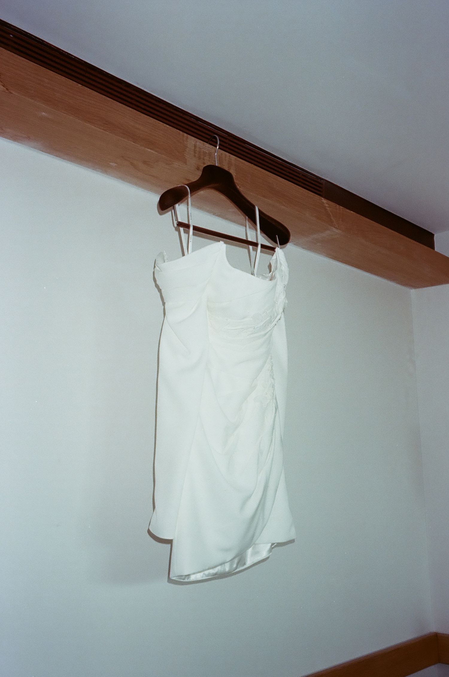 A white sleeveless shirt hangs on a wooden hanger against a plain white wall.