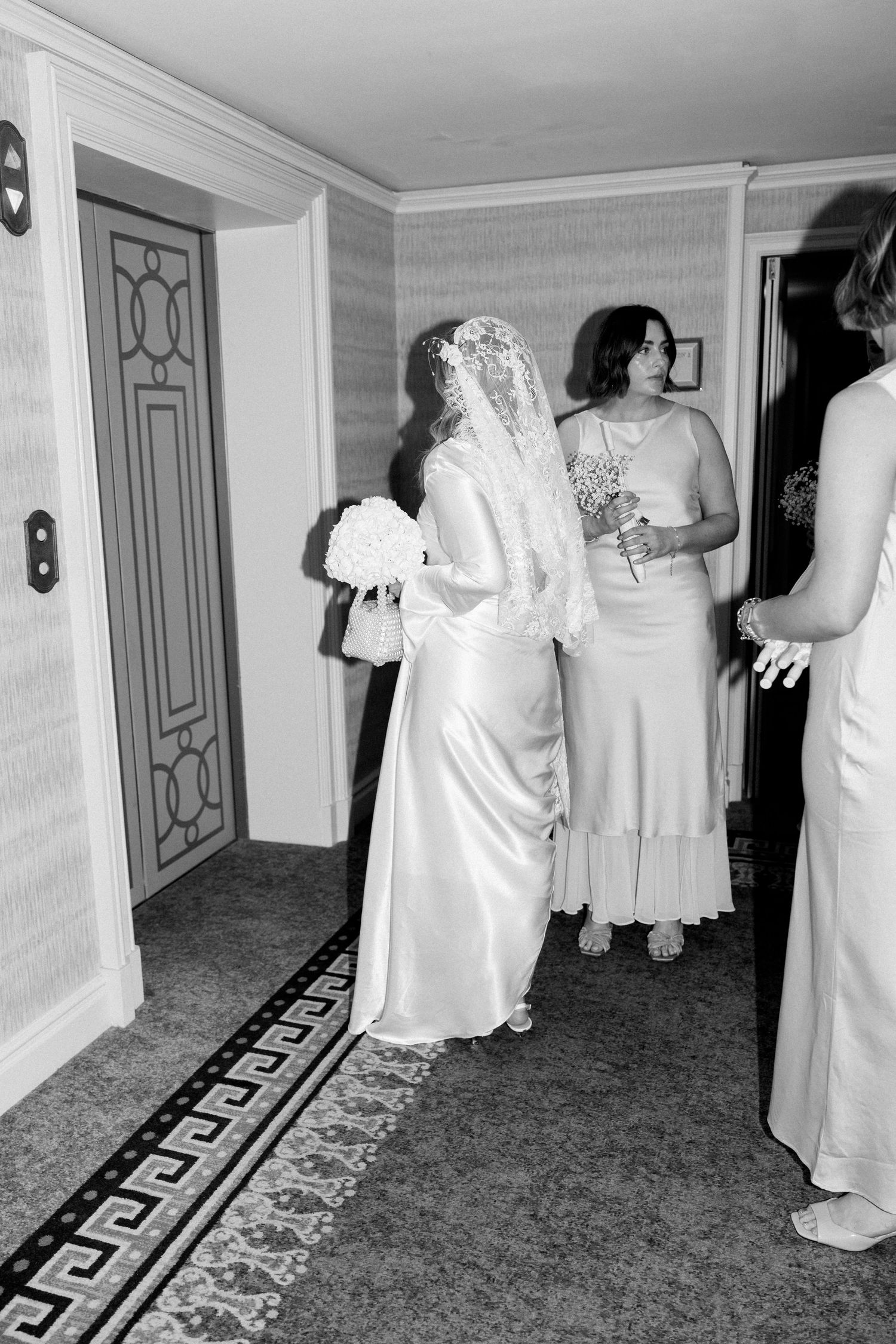 Wedding party in long white dresses gathered in an elegant hallway with ornate doors.