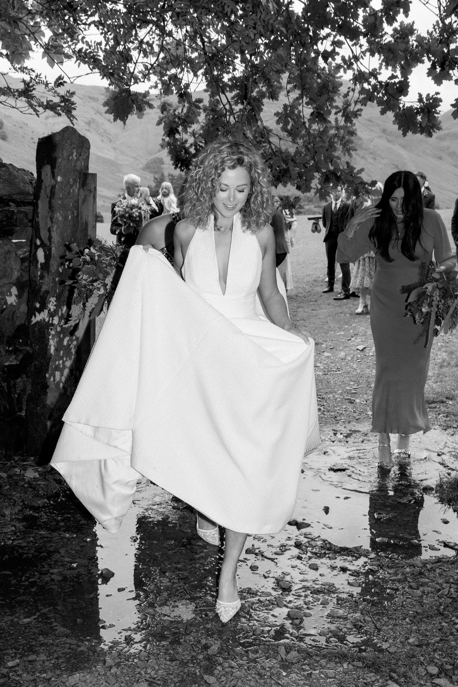 White wedding dress details shown against natural outdoor backdrop with trees and mountains.