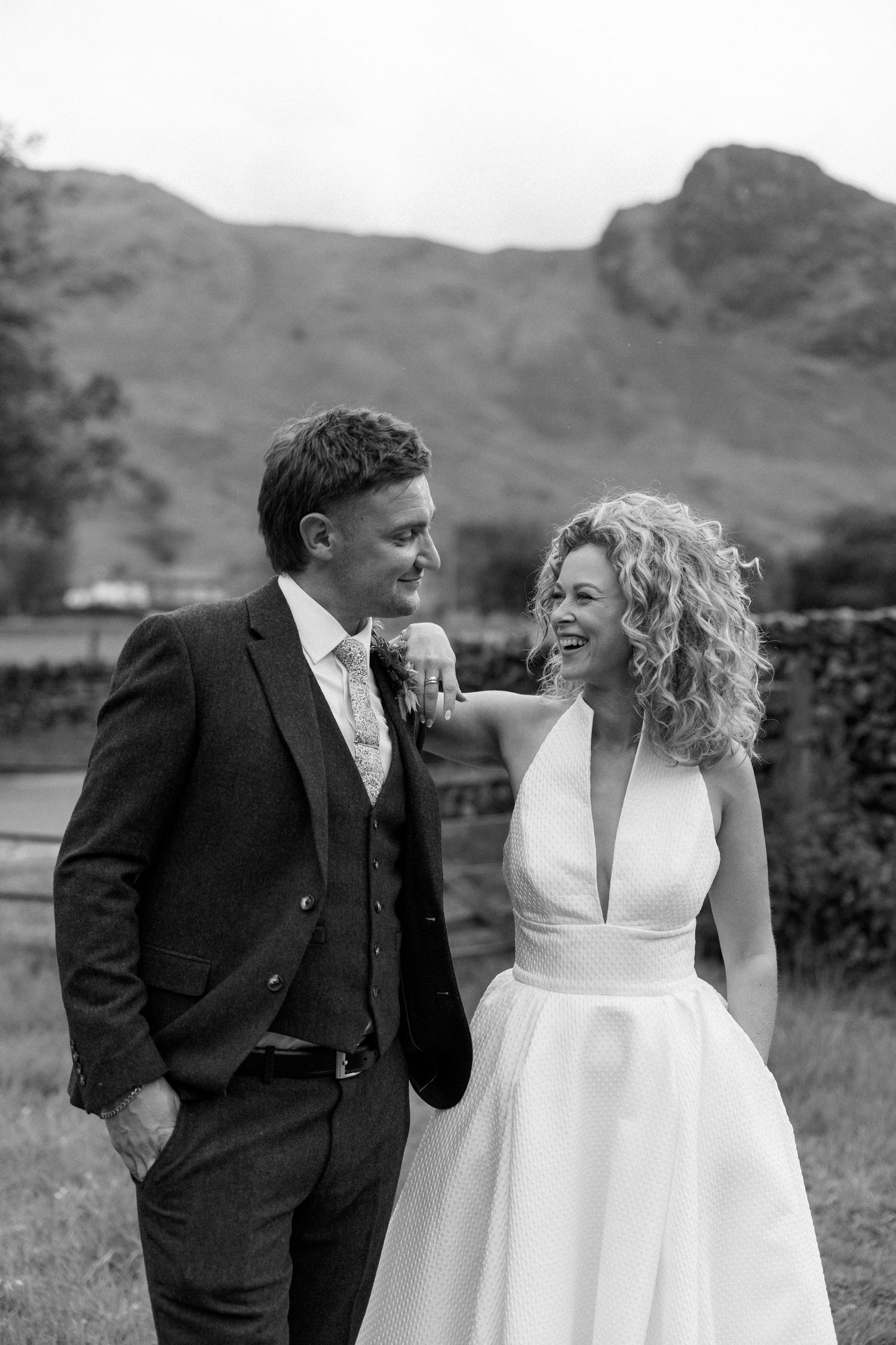 Wedding couple shares a candid moment in a field with mountains in the background.