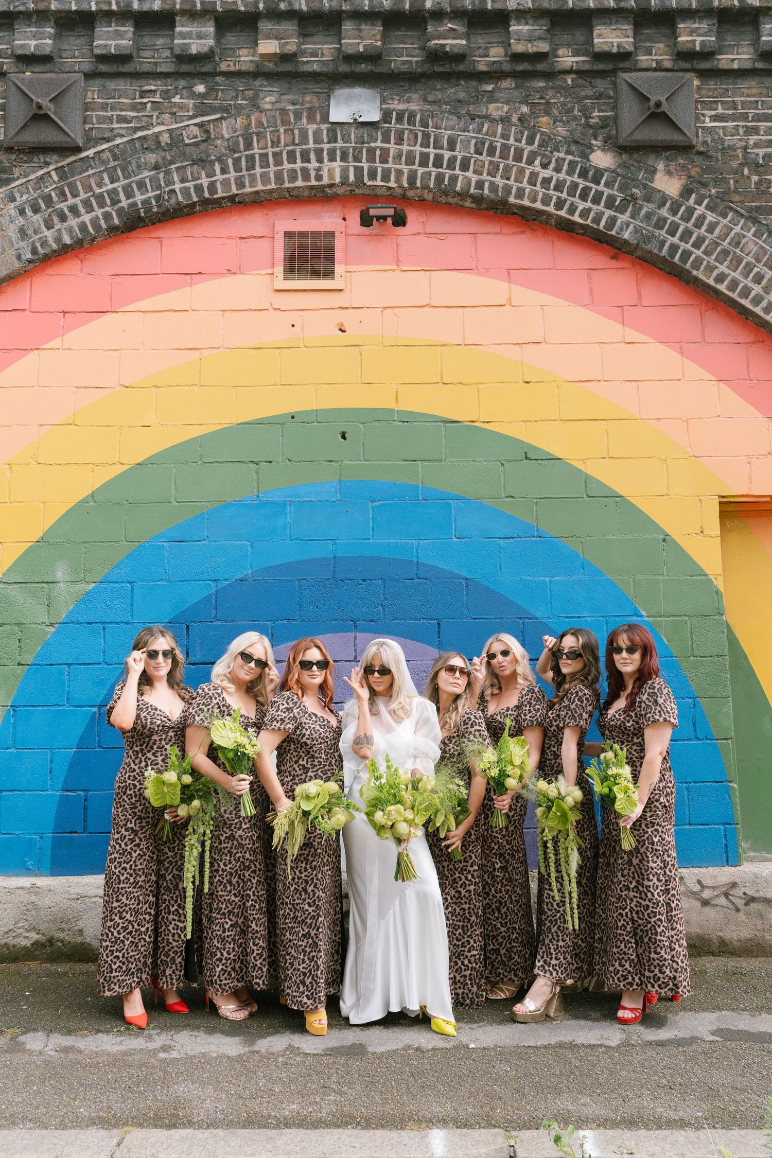 Wedding party poses against colorful rainbow mural wall with leopard print dresses.