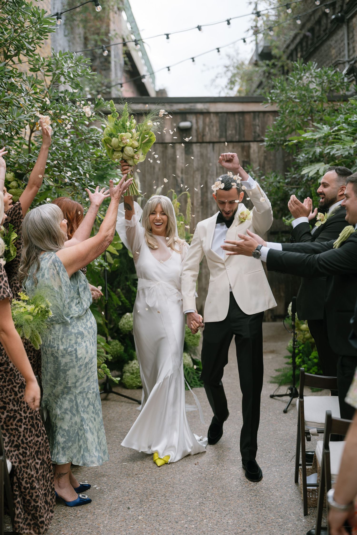 Wedding celebration with guests cheering as couple walks down aisle at outdoor venue.