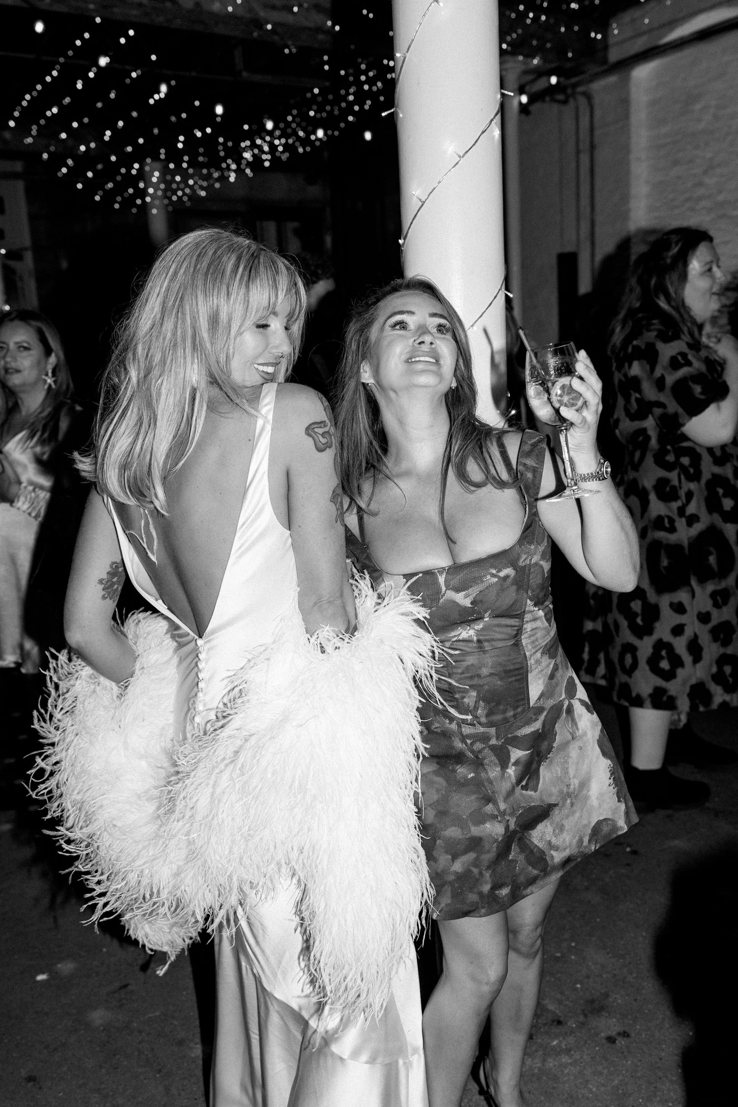Two women dancing under string lights at wedding reception in elegant dresses.