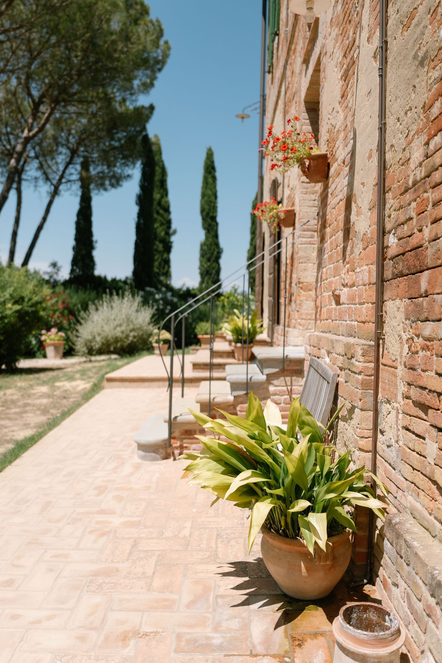 Rustic brick walkway with terracotta pots and cypress trees at an Italian villa.