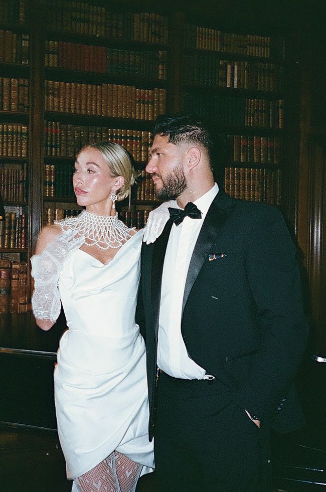 A couple in formal attire dancing together in an elegant library setting with dark wood bookshelves in the background.