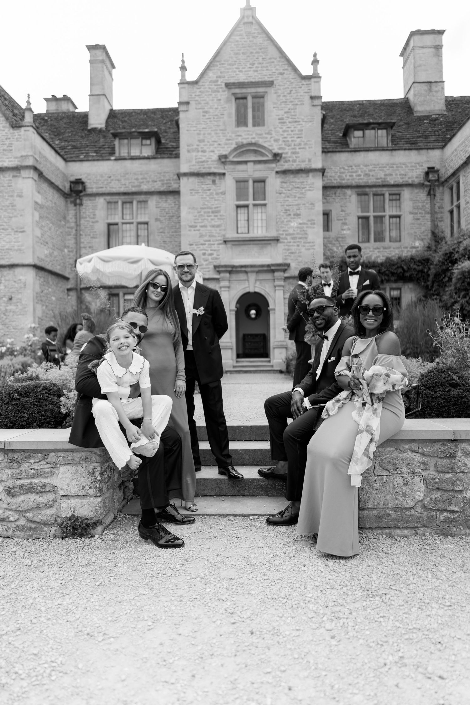 Black and white photo of wedding guests posing in front of a grand stone manor house.