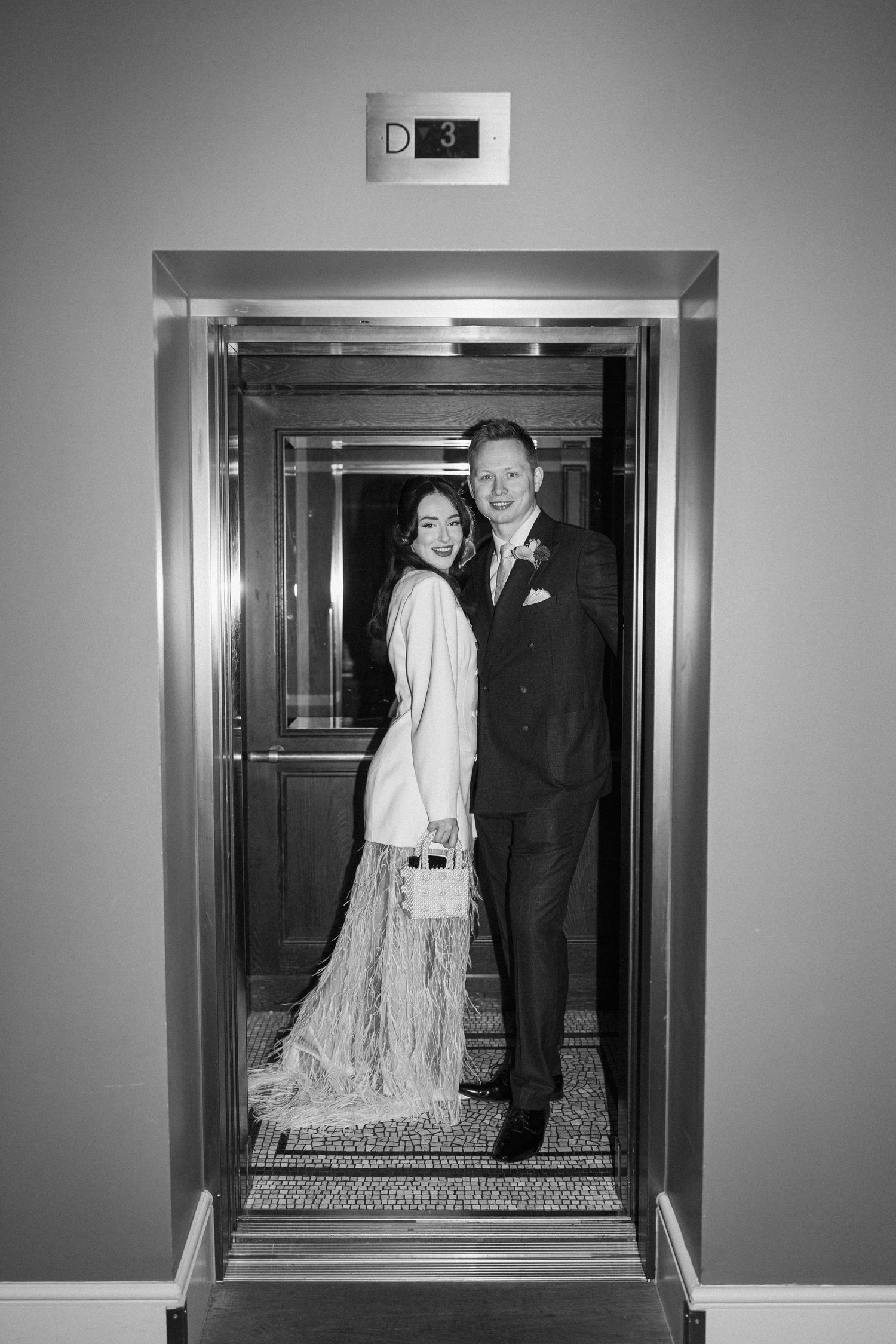 Black and white photo of bride and groom posing together inside an elevator.