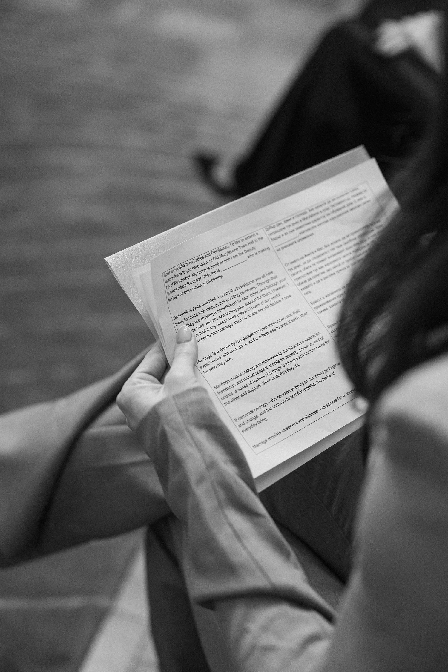 Black and white close-up of wedding guest reading ceremony program during nuptials.