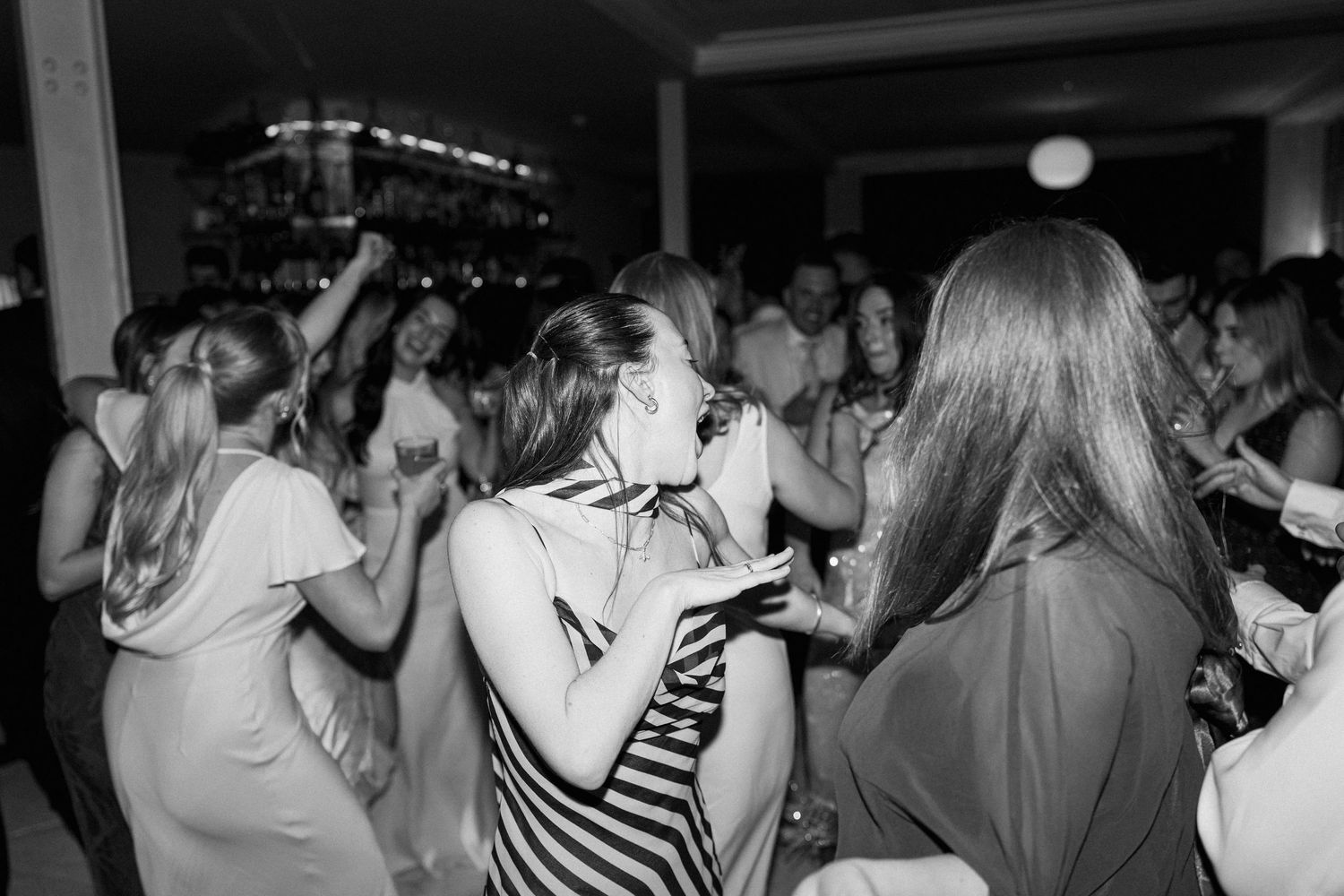 Black and white photo of wedding guests dancing and celebrating at lively evening reception party.