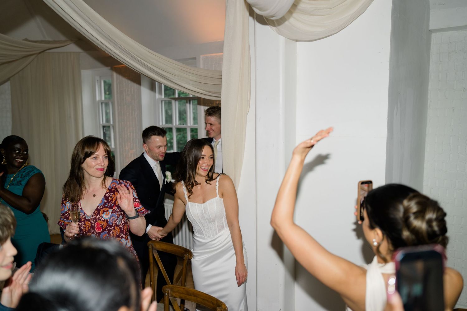 Bride in white dress making a grand entrance at her wedding reception with guests applauding.