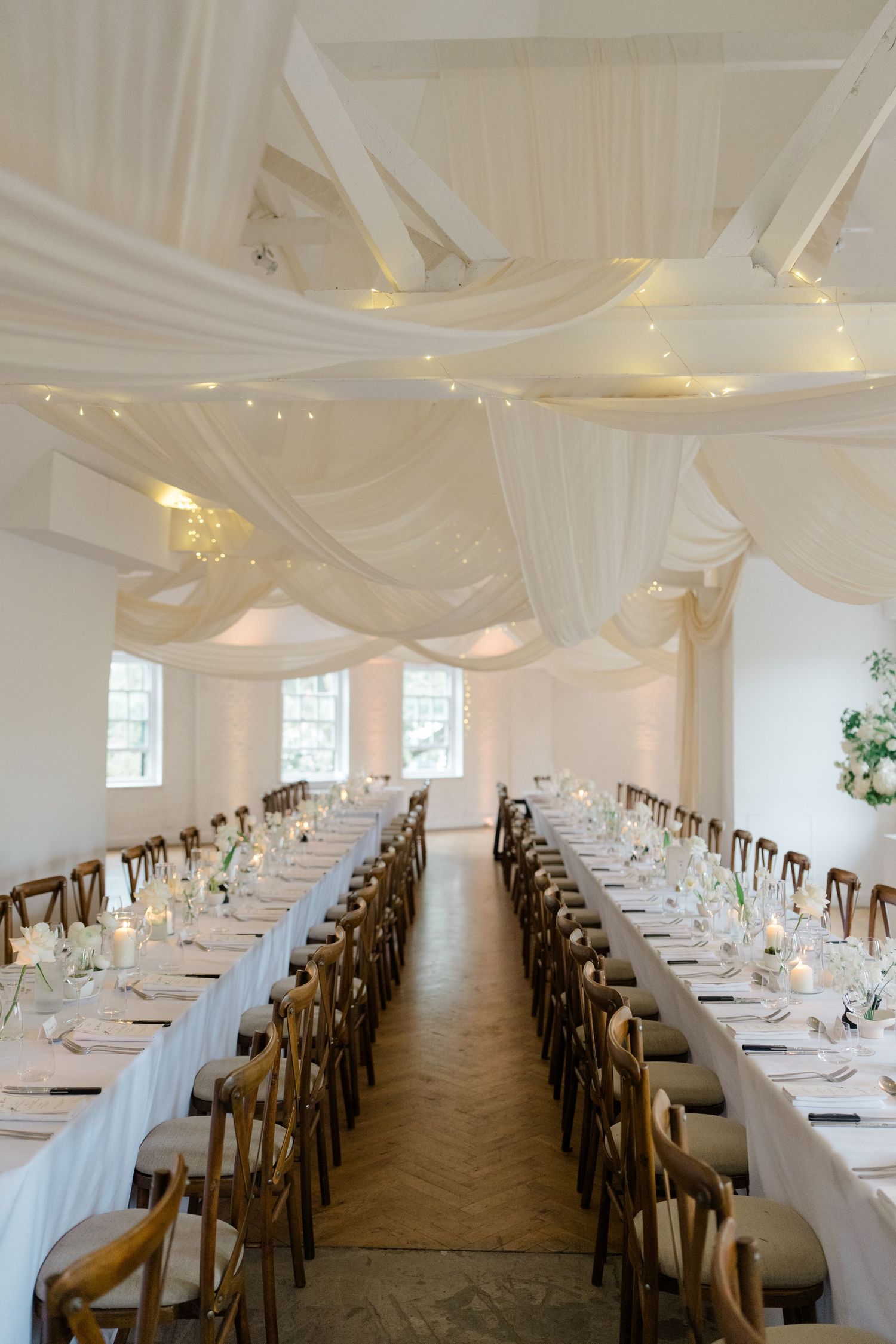 Stunning wedding reception hall with white draped ceiling, fairy lights, and long banquet tables with candles.