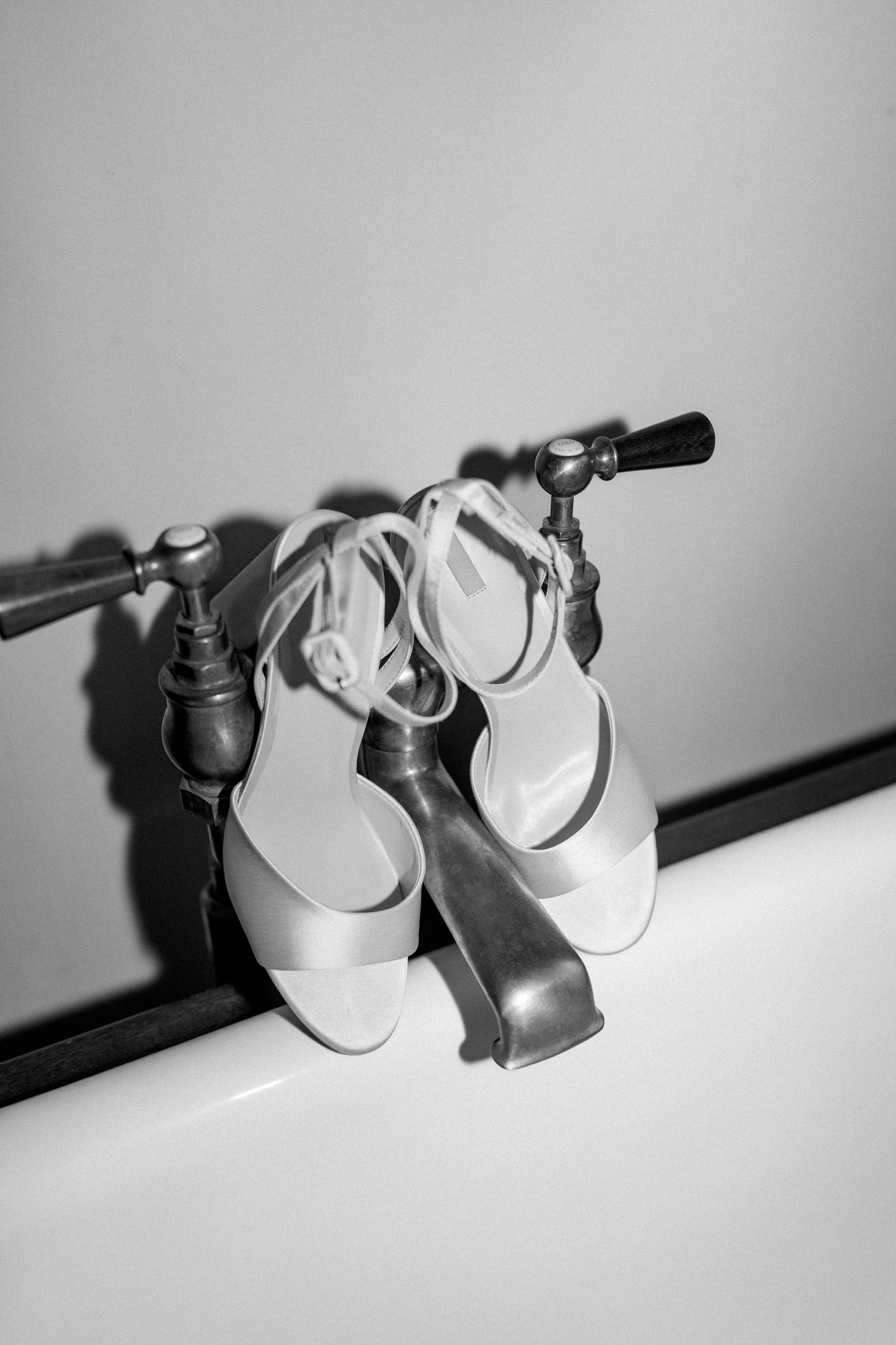 Black and white artistic shot of white wedding shoes hanging on a metal rail.