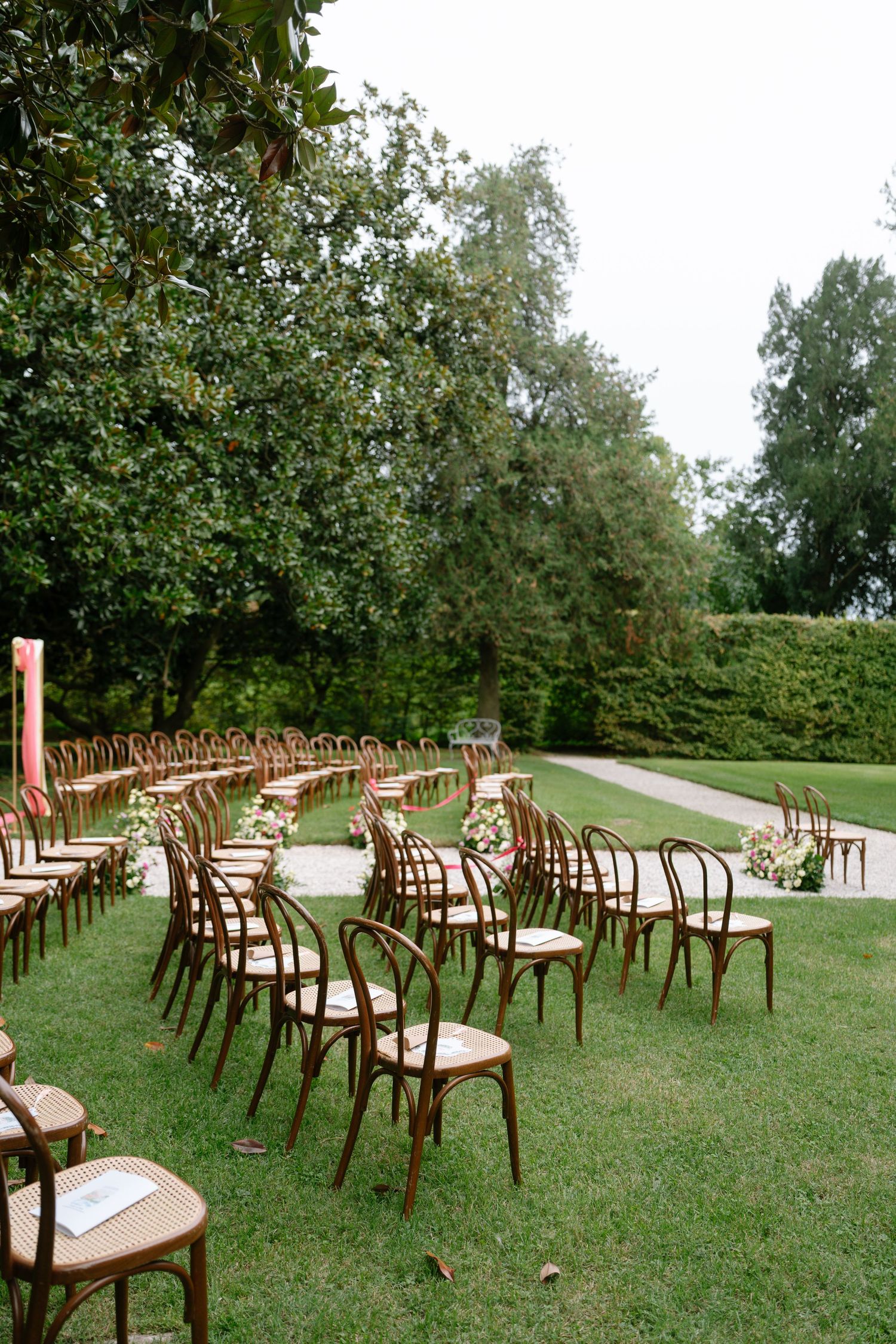 Wooden cross-back chairs set up in neat rows on a green lawn for an outdoor ceremony.