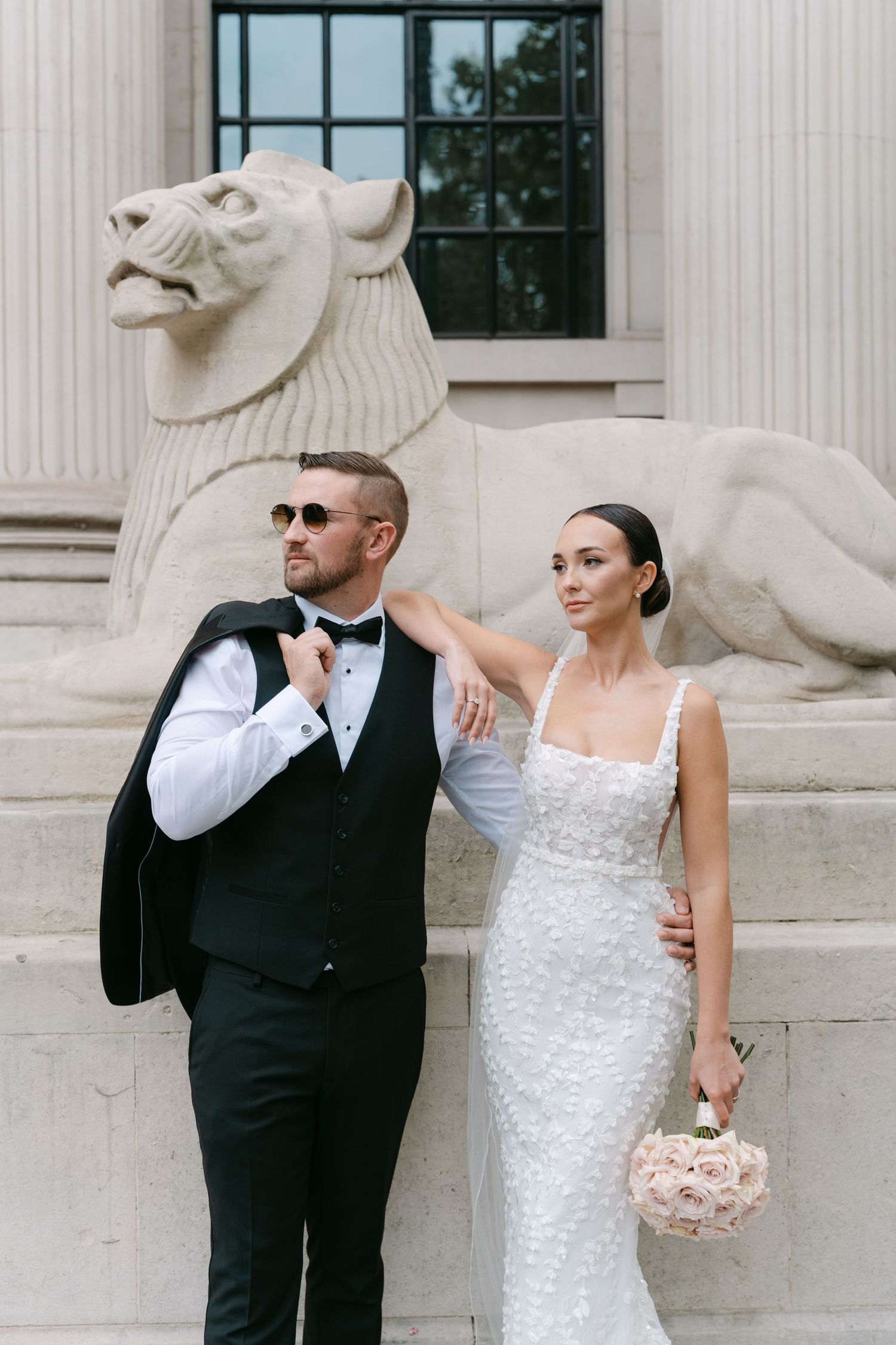 Elegant wedding couple poses near stone lions at a historic building entrance.