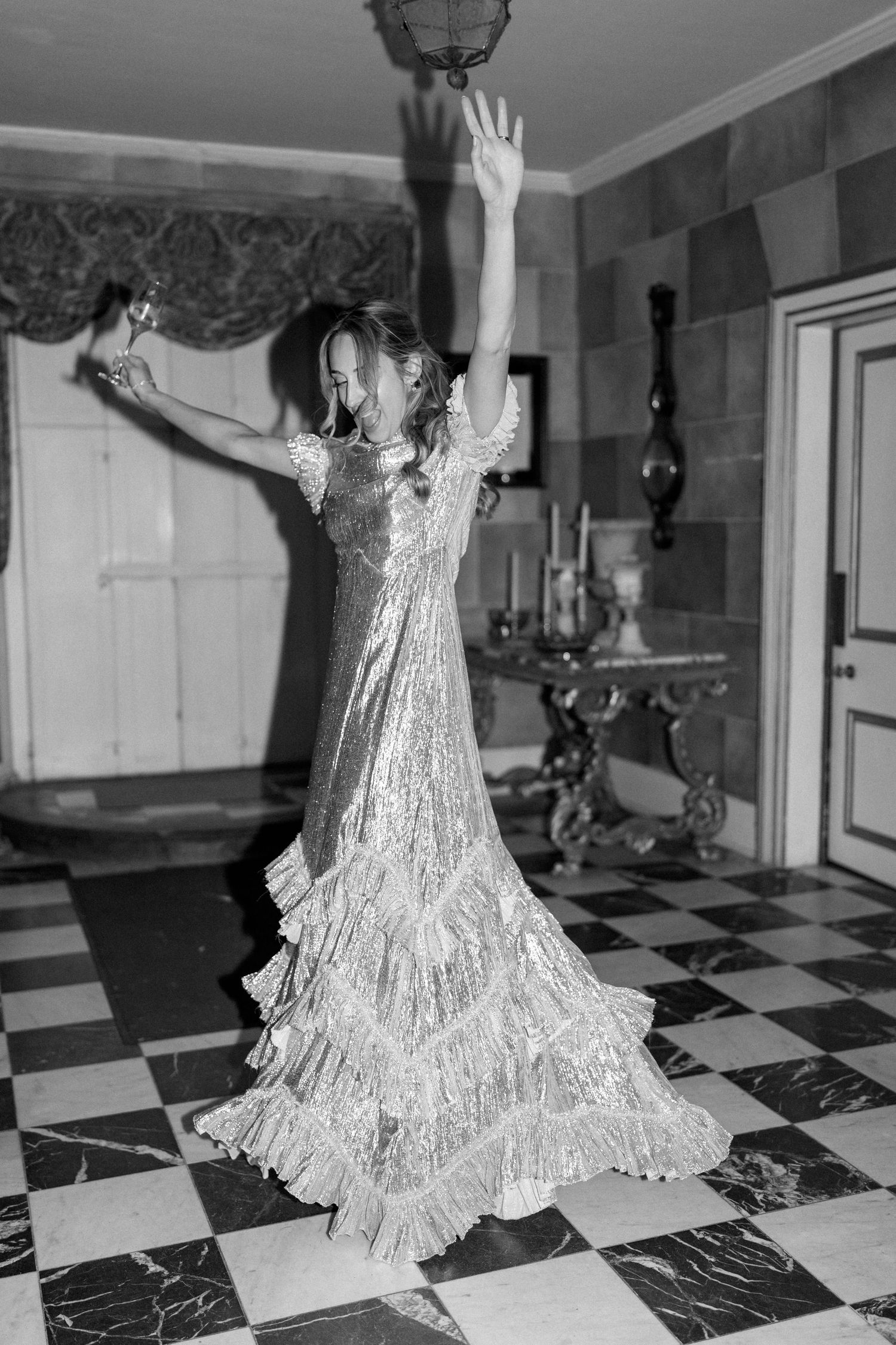 A figure in a metallic dress performs expressive movements on a checkerboard marble floor.