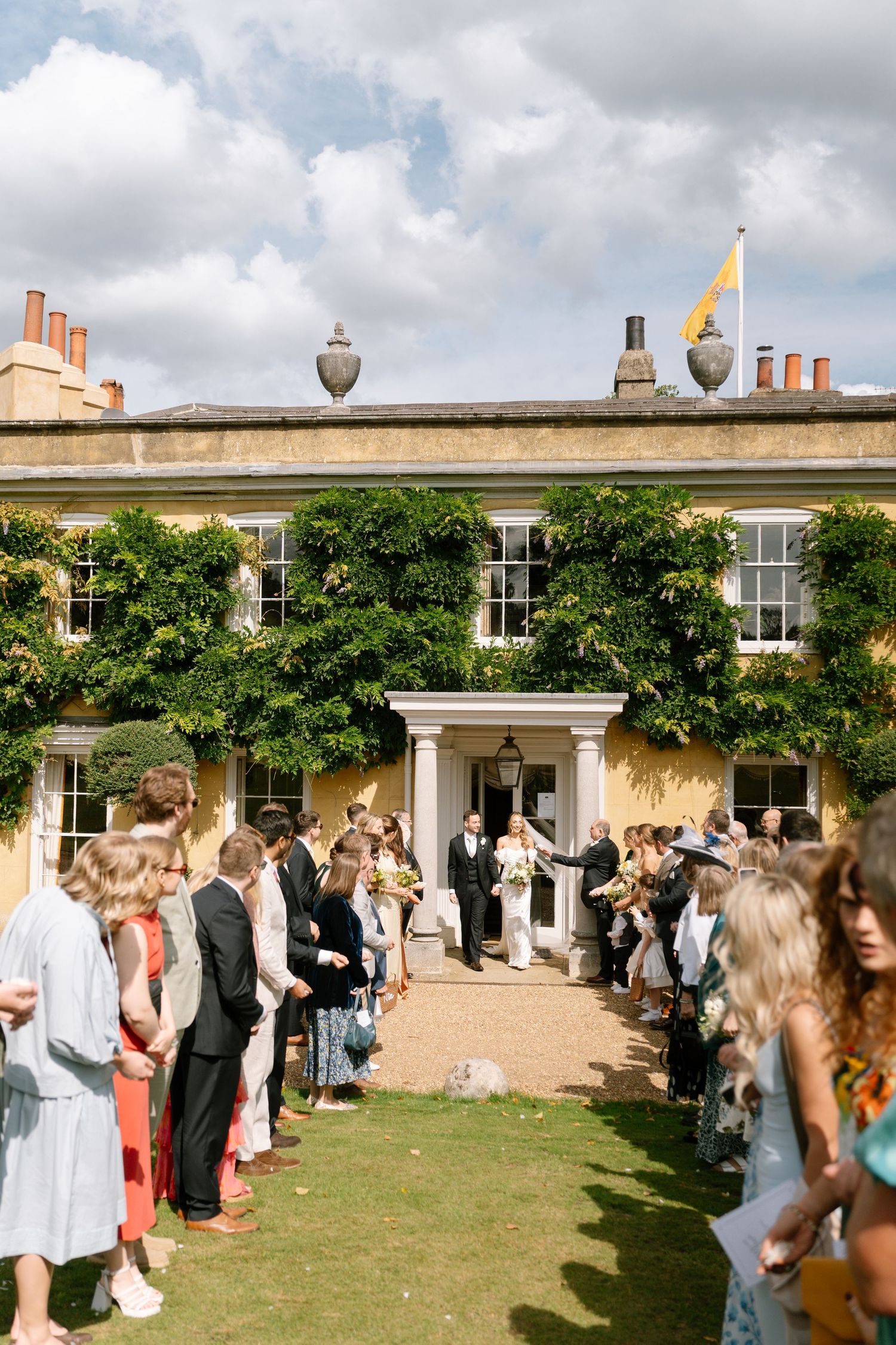 Wedding guests gather on a lawn outside a stately building for the celebration.
