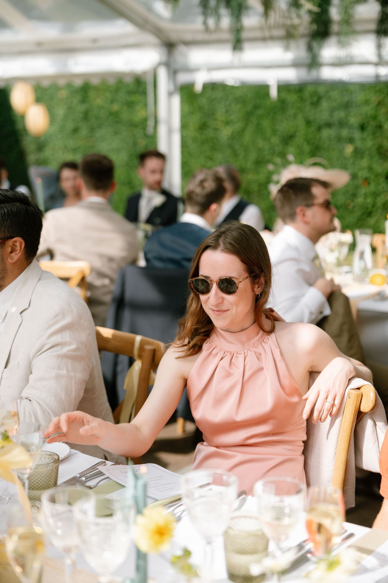Guest in pink dress and sunglasses seated at elegant outdoor reception.