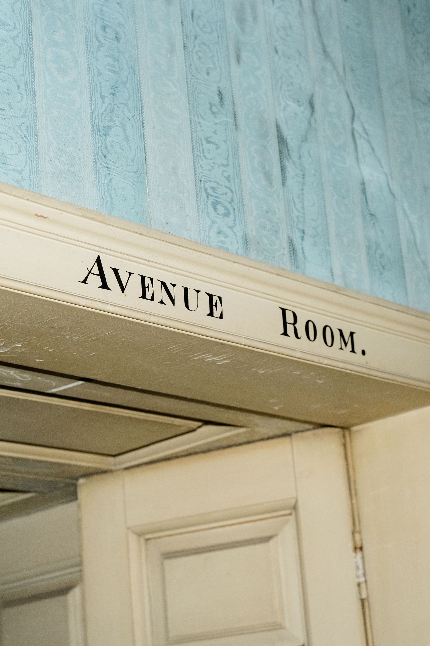 Vintage cream doorway sign reading Avenue Room with blue patterned wallpaper in a historic English estate.