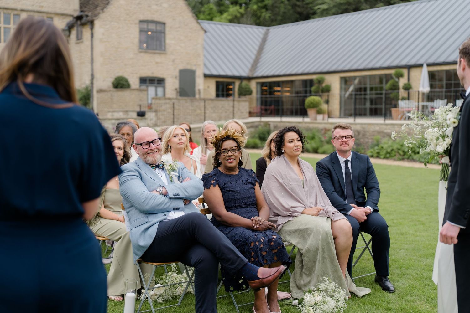 Wedding guests smiling and seated at an elegant outdoor ceremony at a Cotswolds estate venue.