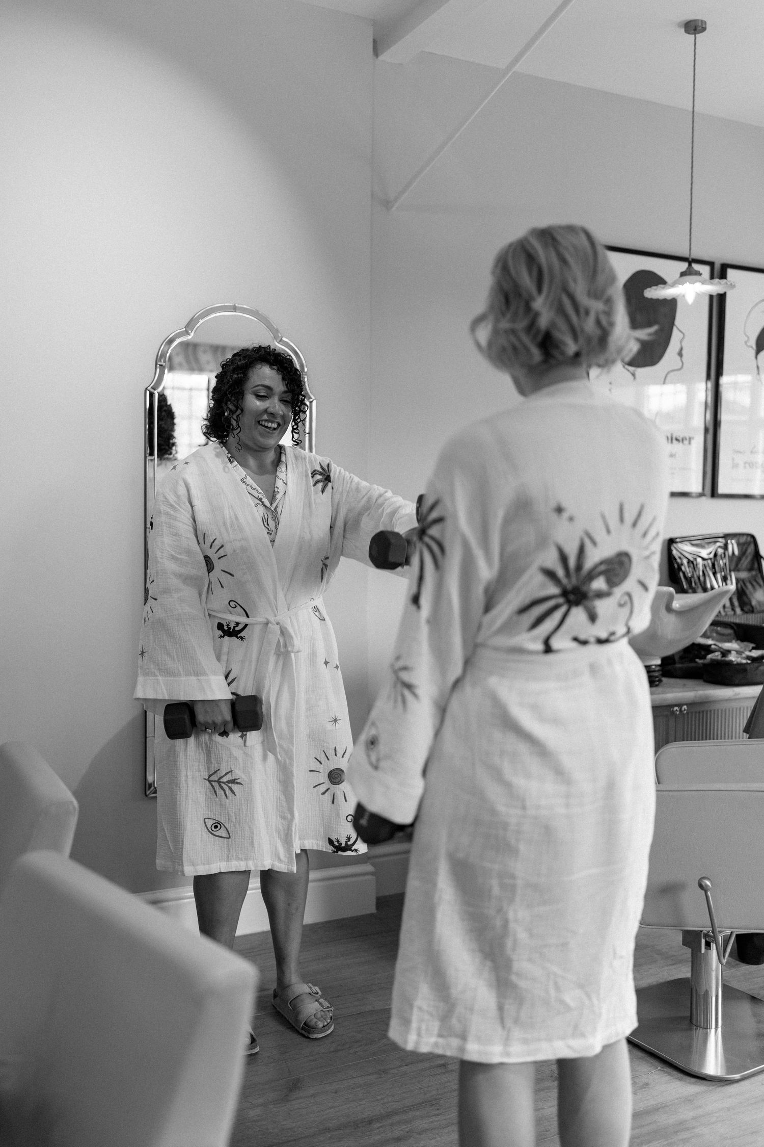 Two bridesmaids in matching robes laugh together while getting ready for a wedding.