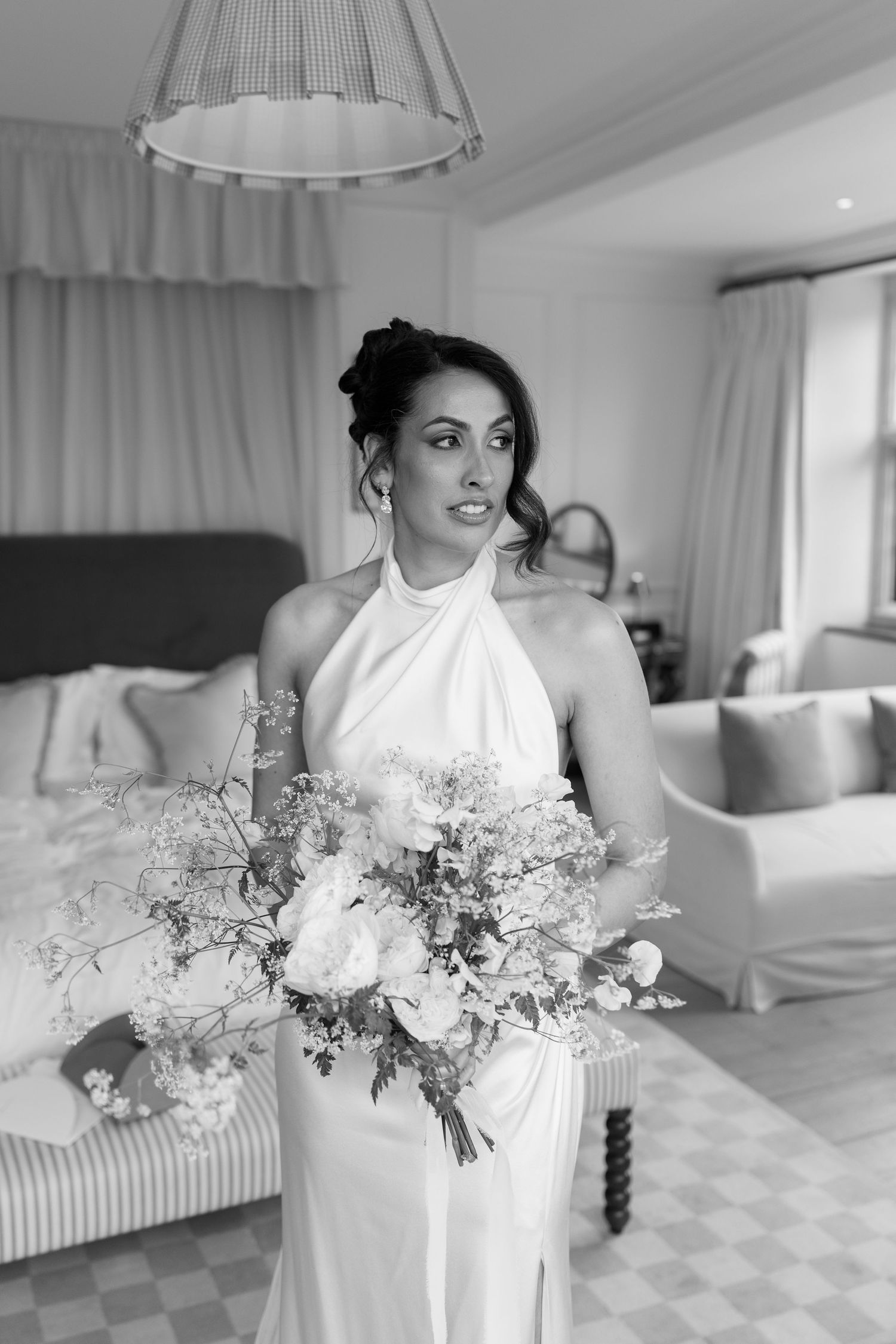 Black and white portrait of bride in halter neck gown holding a large white floral bouquet indoors.