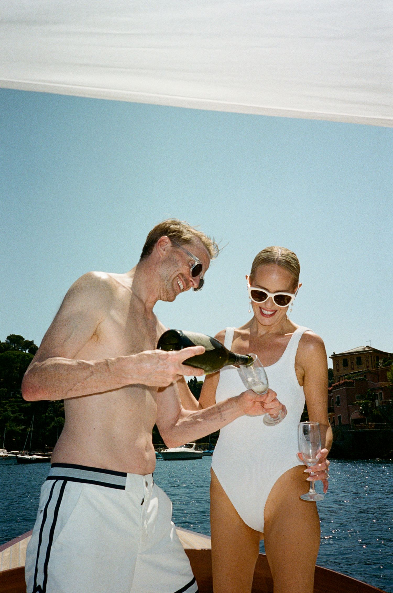 Couple in swimwear on a boat pouring champagne, enjoying a sunny summer day on the water.