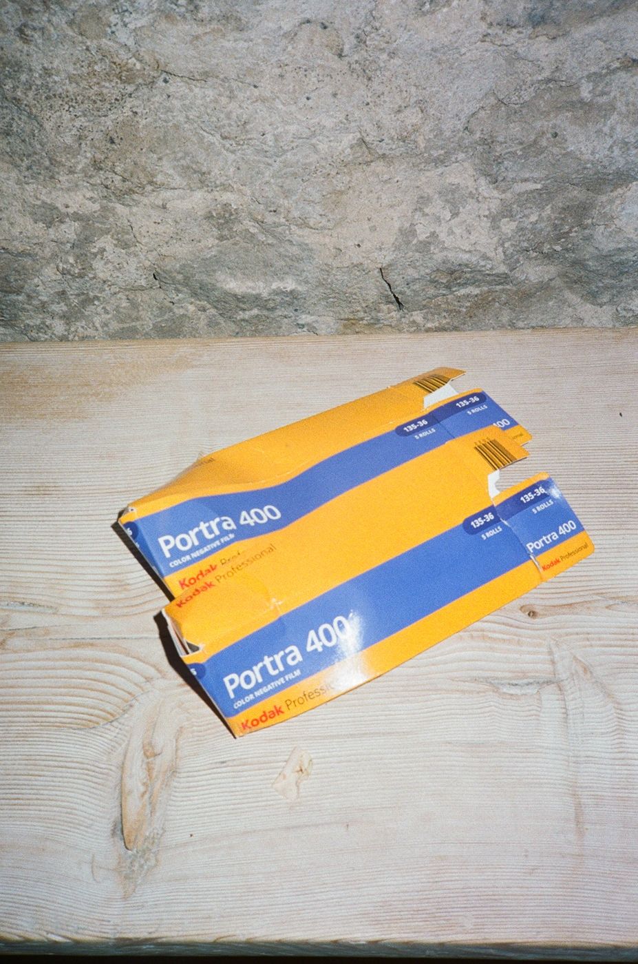 Two boxes of Kodak Portra 400 film on a wooden surface against a stone wall.