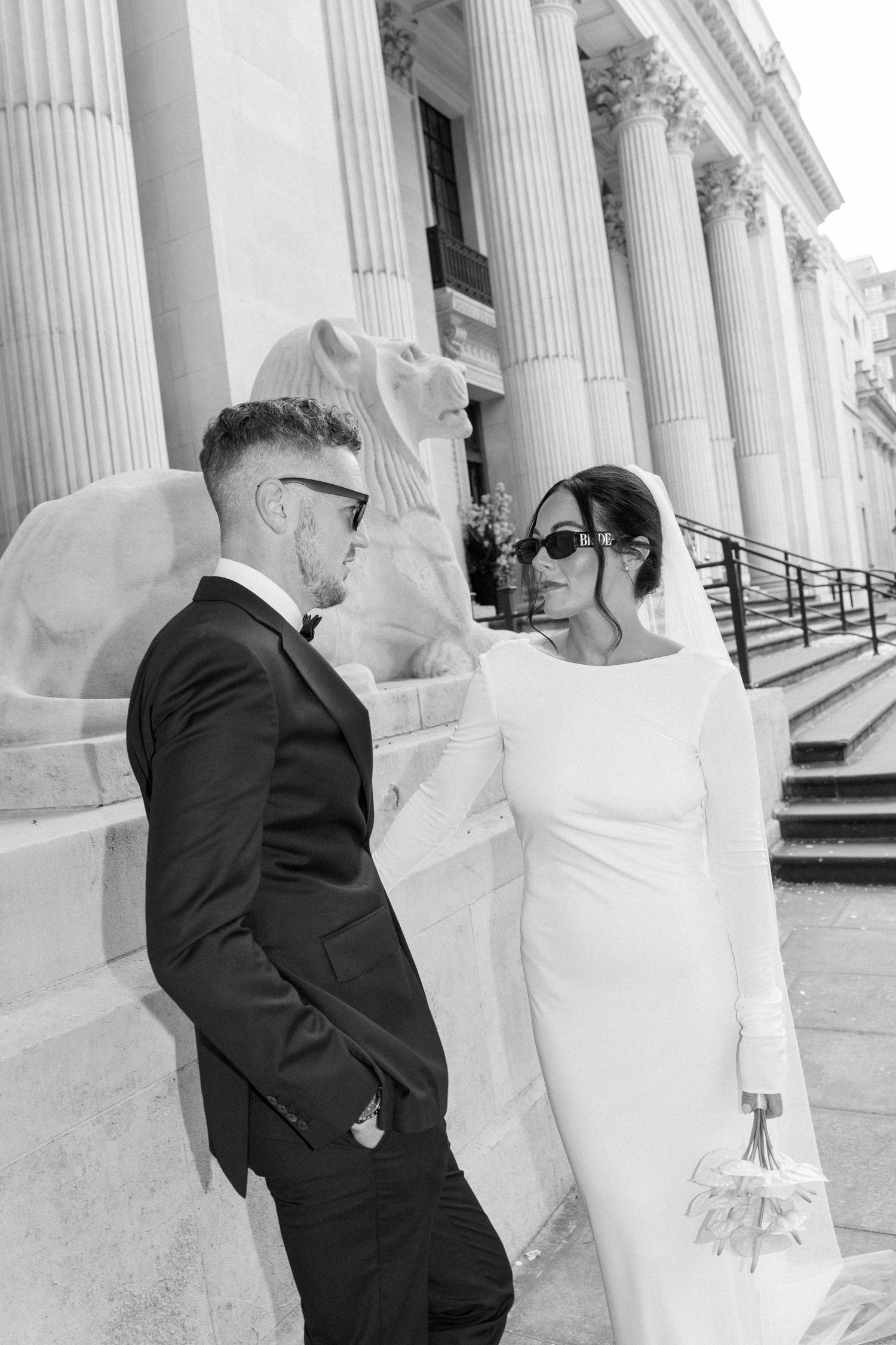 Black and white wedding photo with couple posing against classical colonnade.