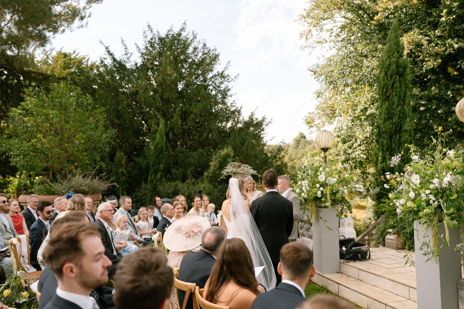 Wedding guests gather on a garden terrace during an outdoor celebration.