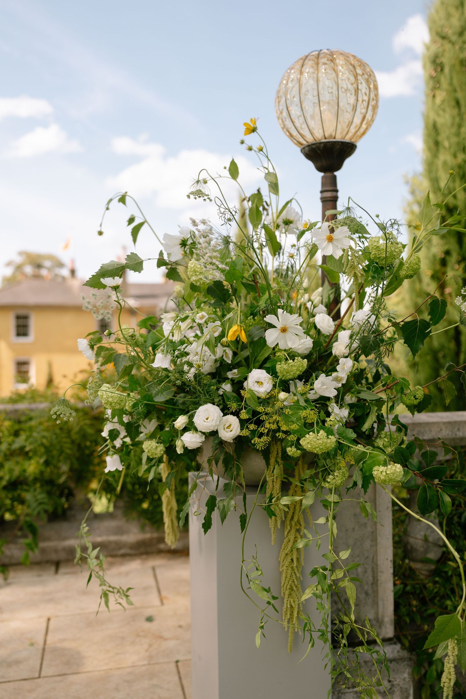 Decorative stone pillars adorned with white floral arrangements and glass globe ornaments.