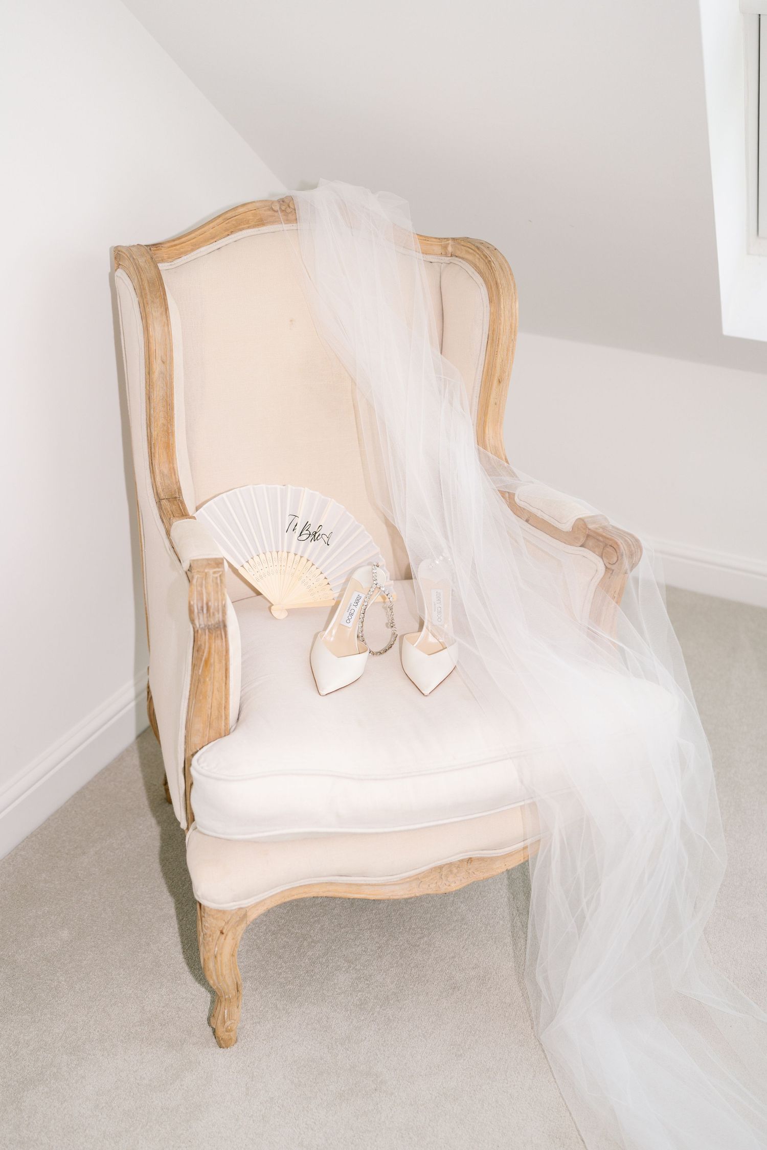 Elegant cream-colored armchair with white tulle veil and bridal shoes arranged on it.