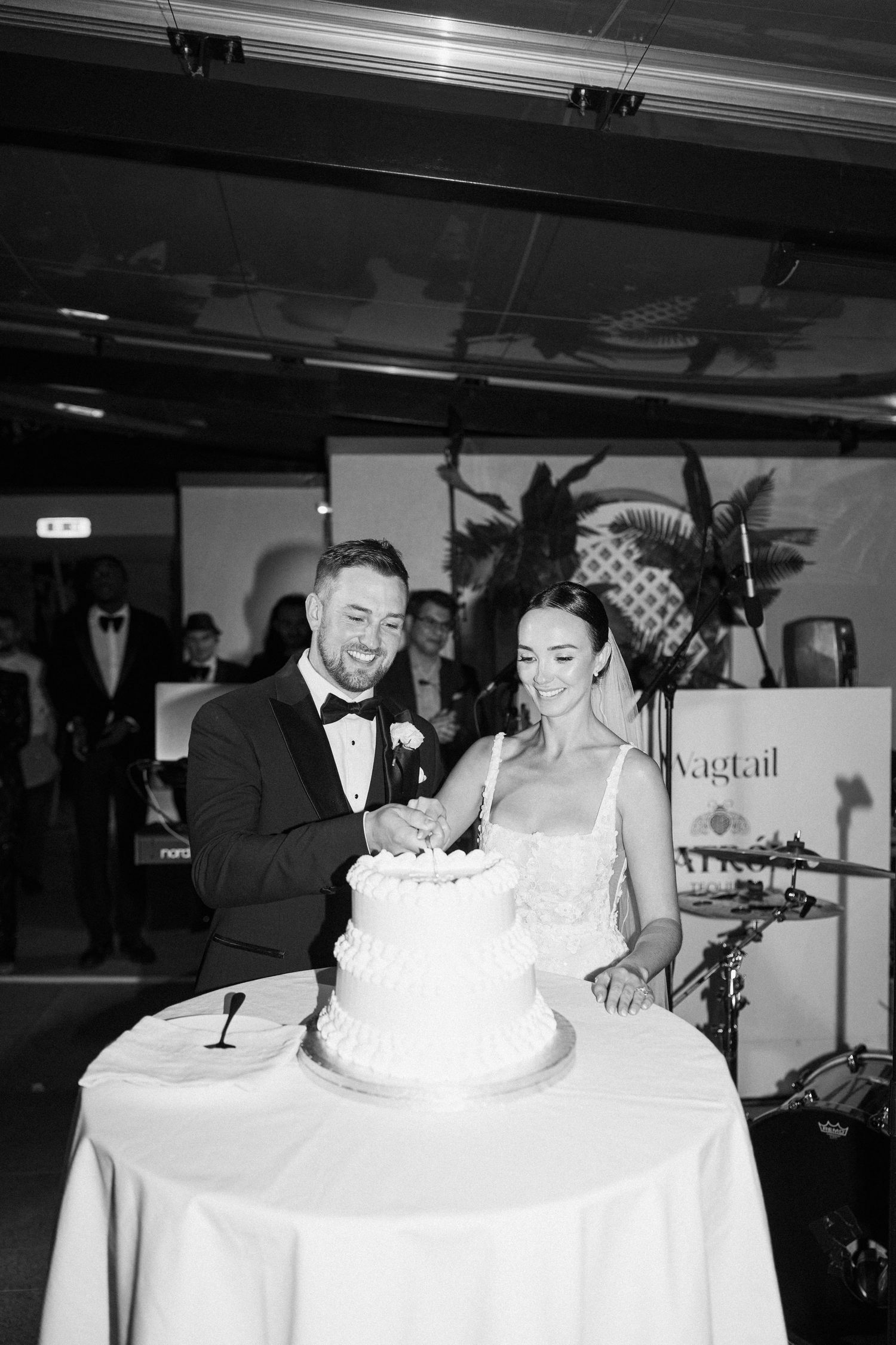 Black and white photo of a couple sharing a joyful moment while cutting their wedding cake.
