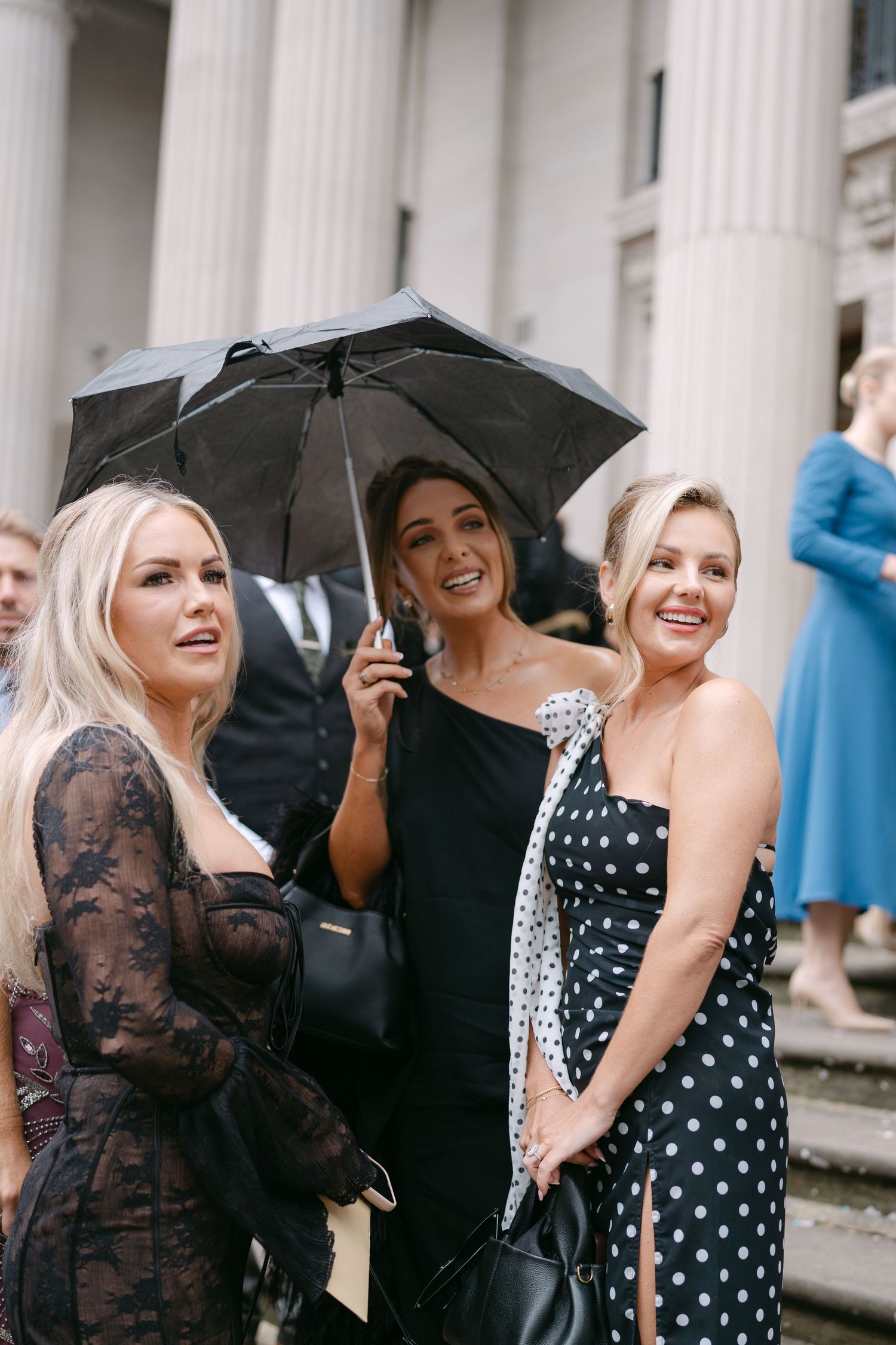 Wedding party with black umbrellas gathered in front of classical white columns.
