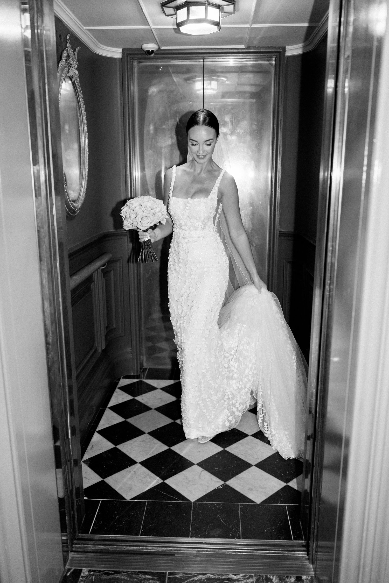 Bride in white dress walks through hallway with black and white checkered floor.
