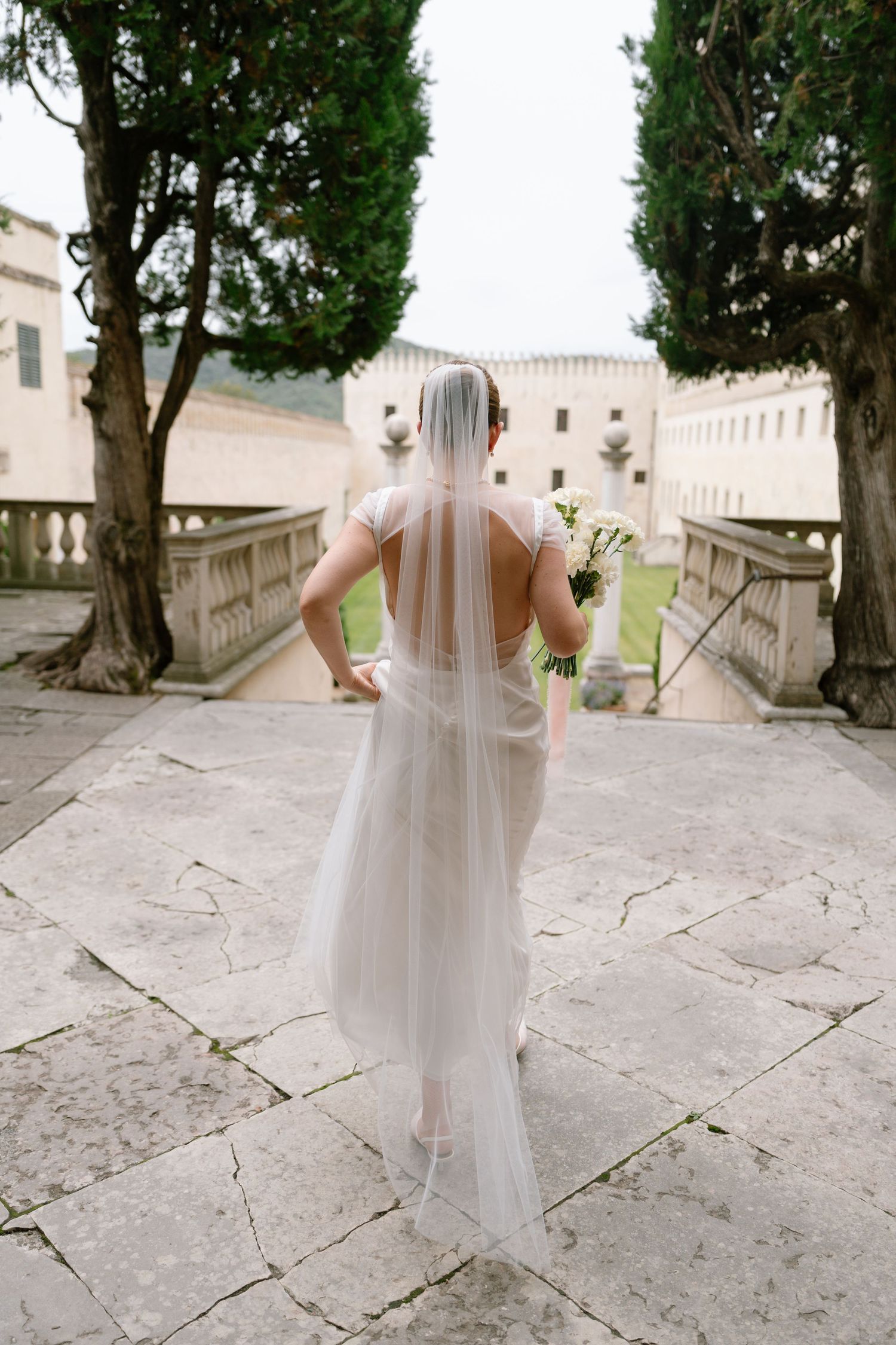 Wedding party members walk down stone pathways at an elegant historic venue.