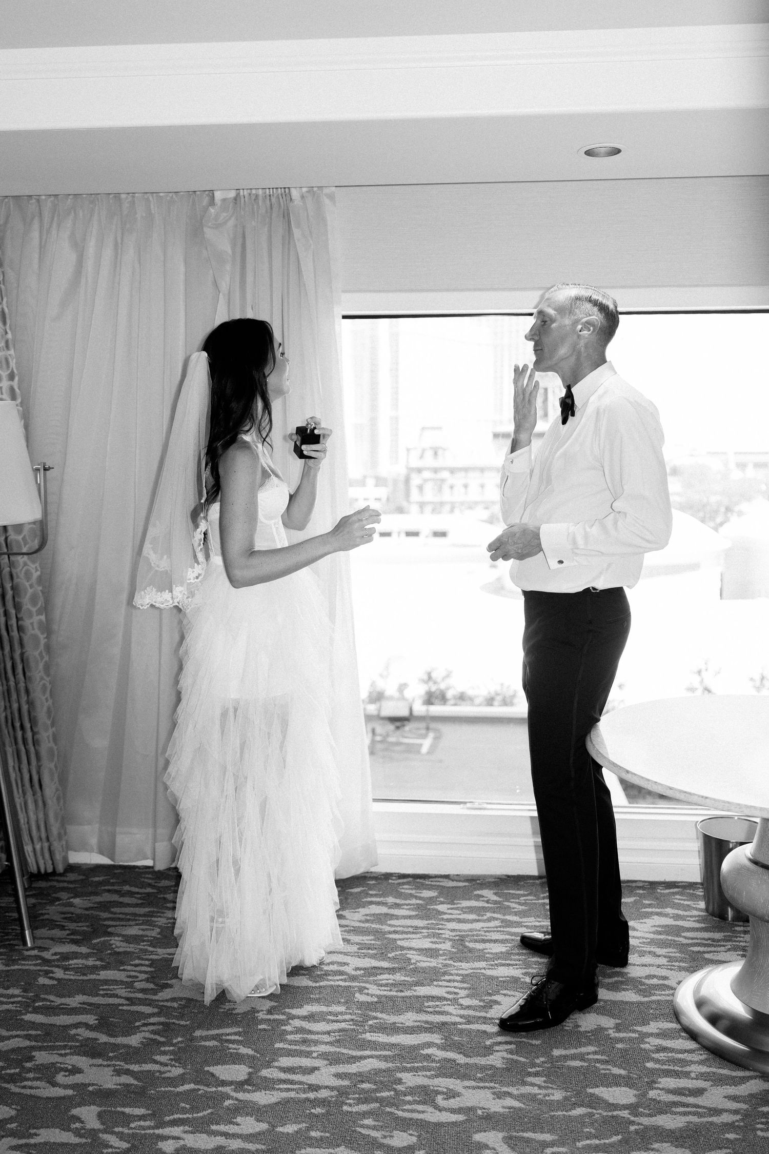 Candid moment between couple in hotel room with city view.