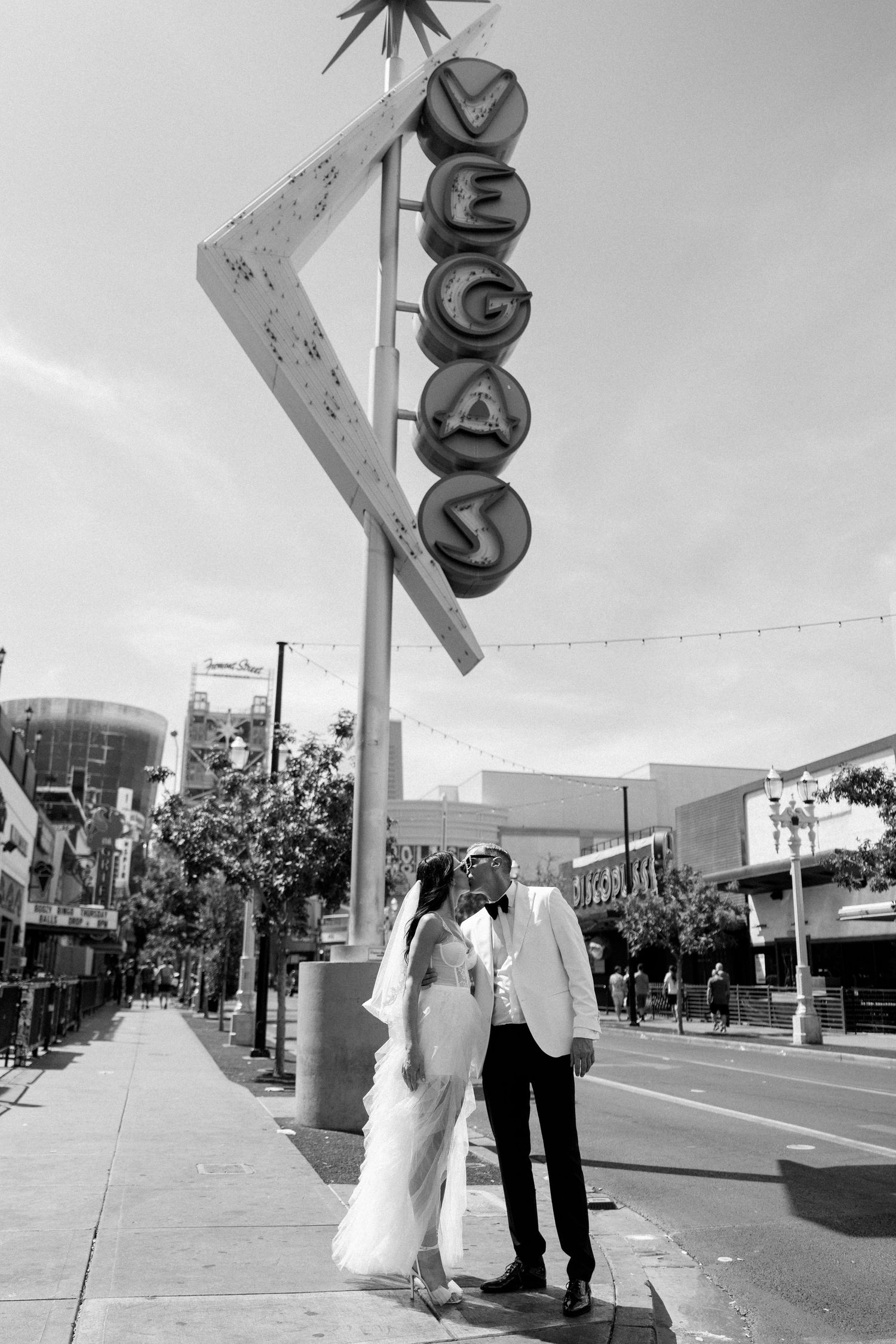 Wedding couple poses beneath iconic retro Vegas sign on urban street.