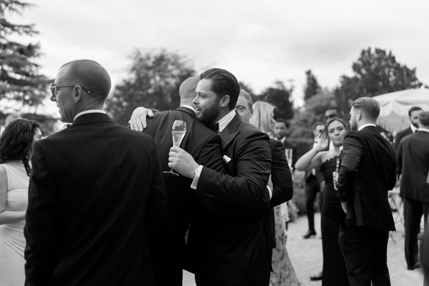Guests in formal attire socializing outdoors at wedding reception on sunny day.
