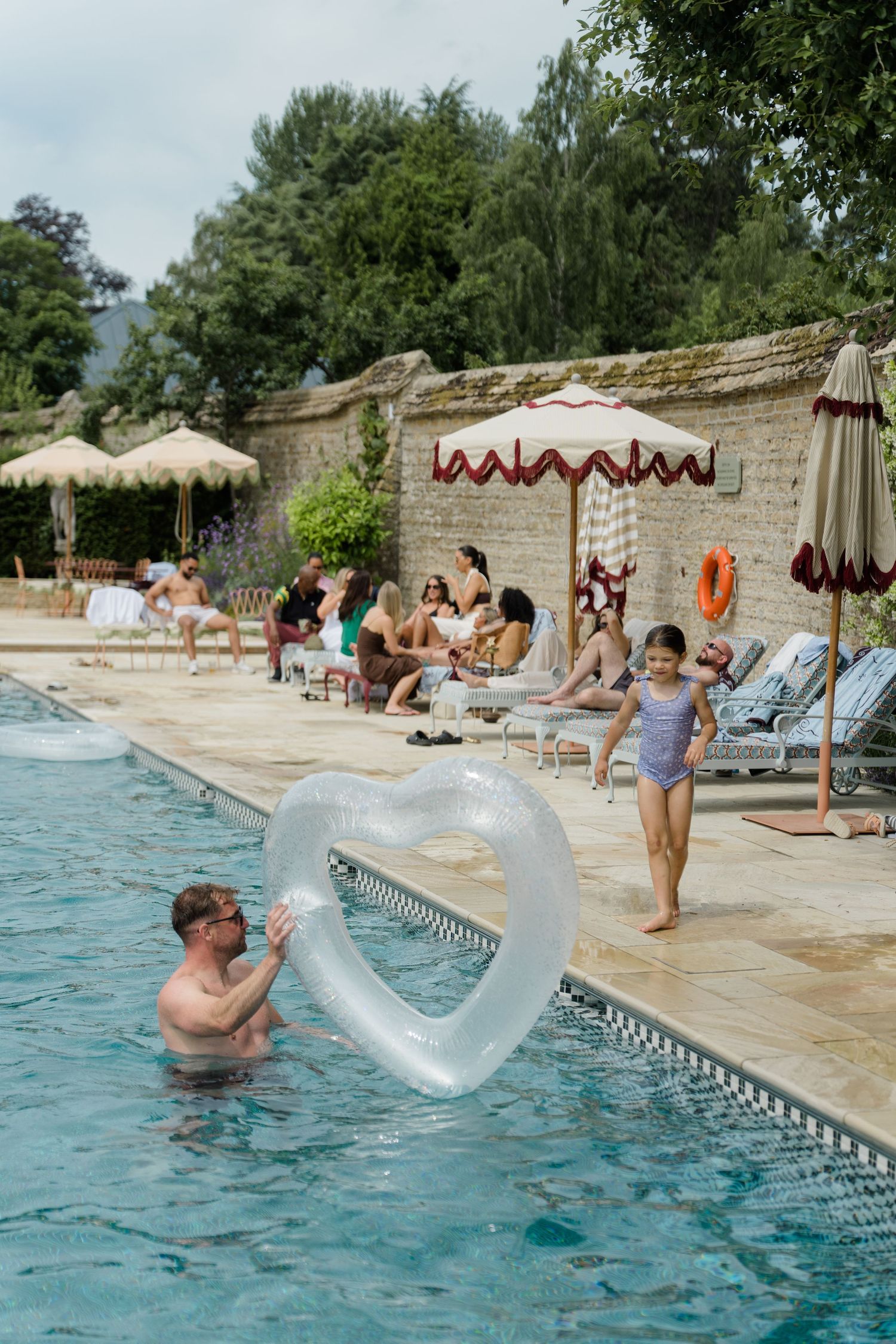 Family enjoying luxury outdoor pool with heart-shaped float at English country wedding venue.