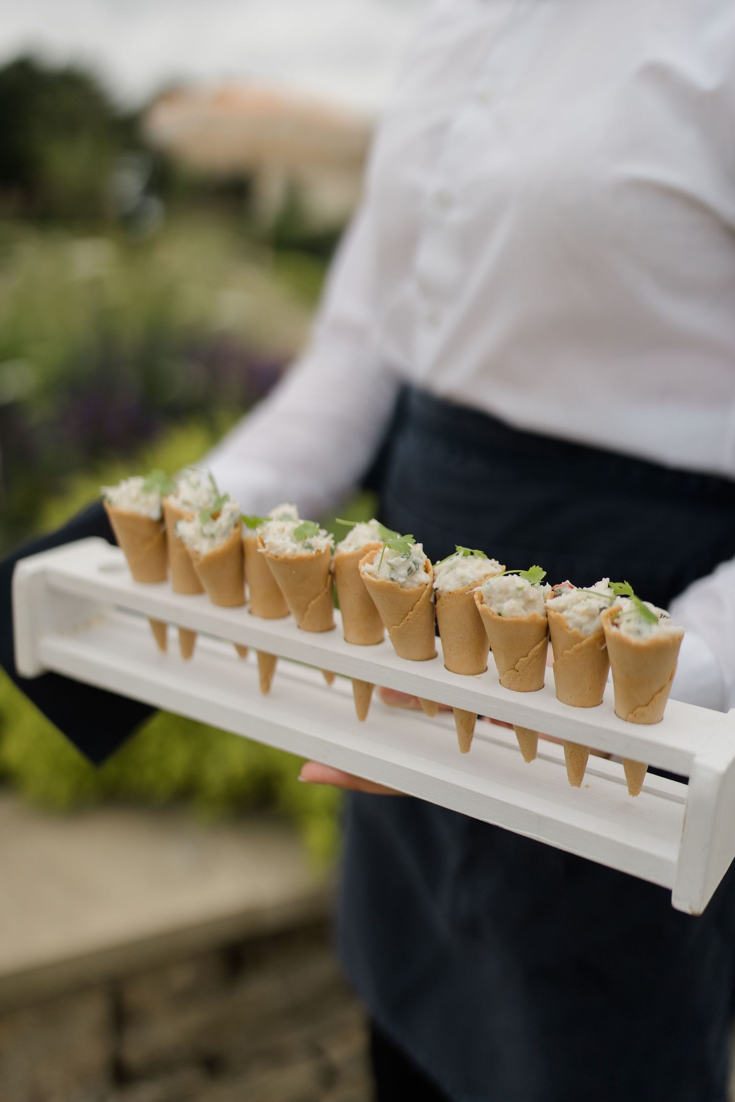 Waiter presenting tray of savory cone appetizers at outdoor wedding reception catering.