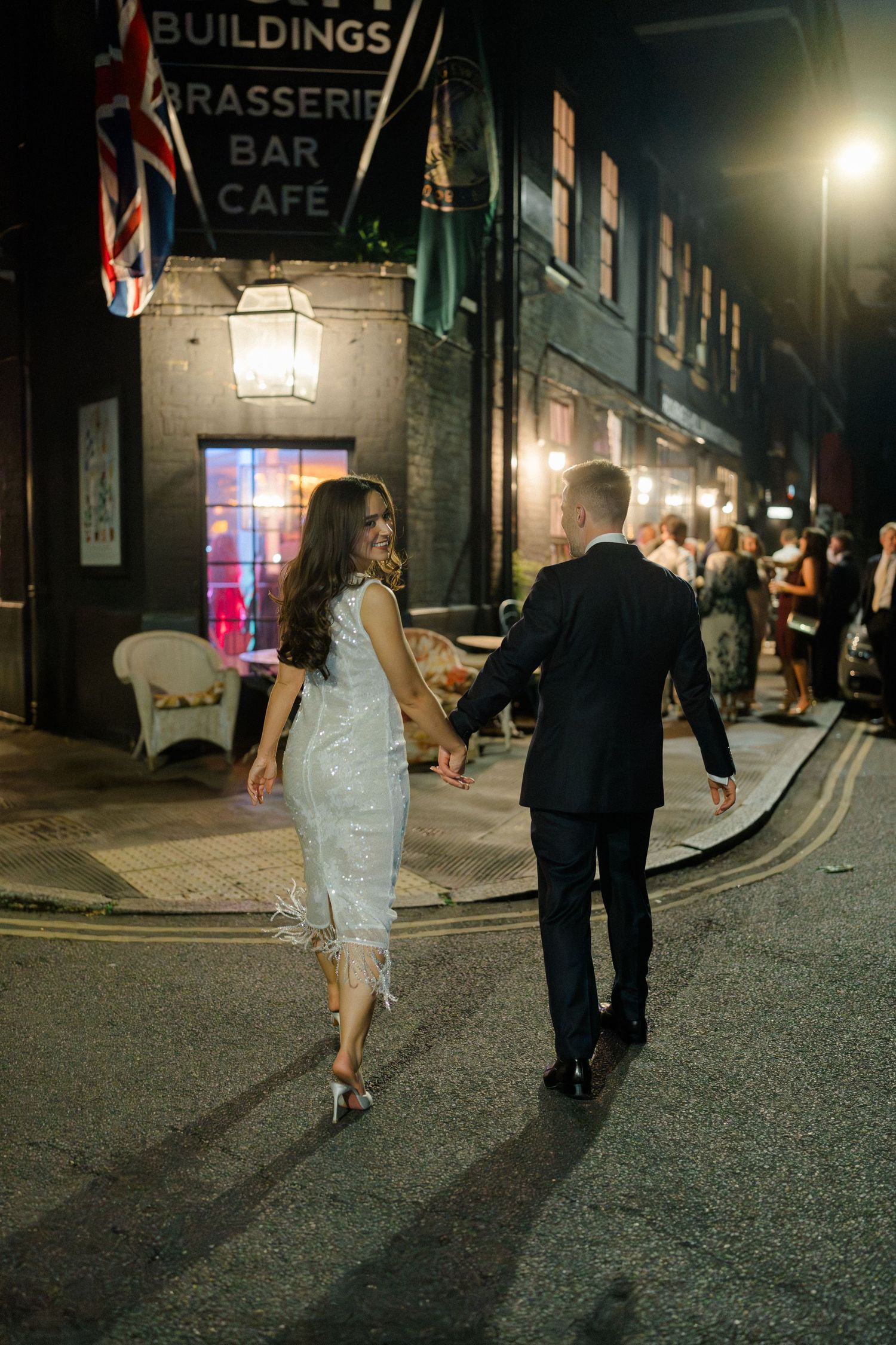 Bride and groom walking hand in hand outside brasserie bar cafe at night.