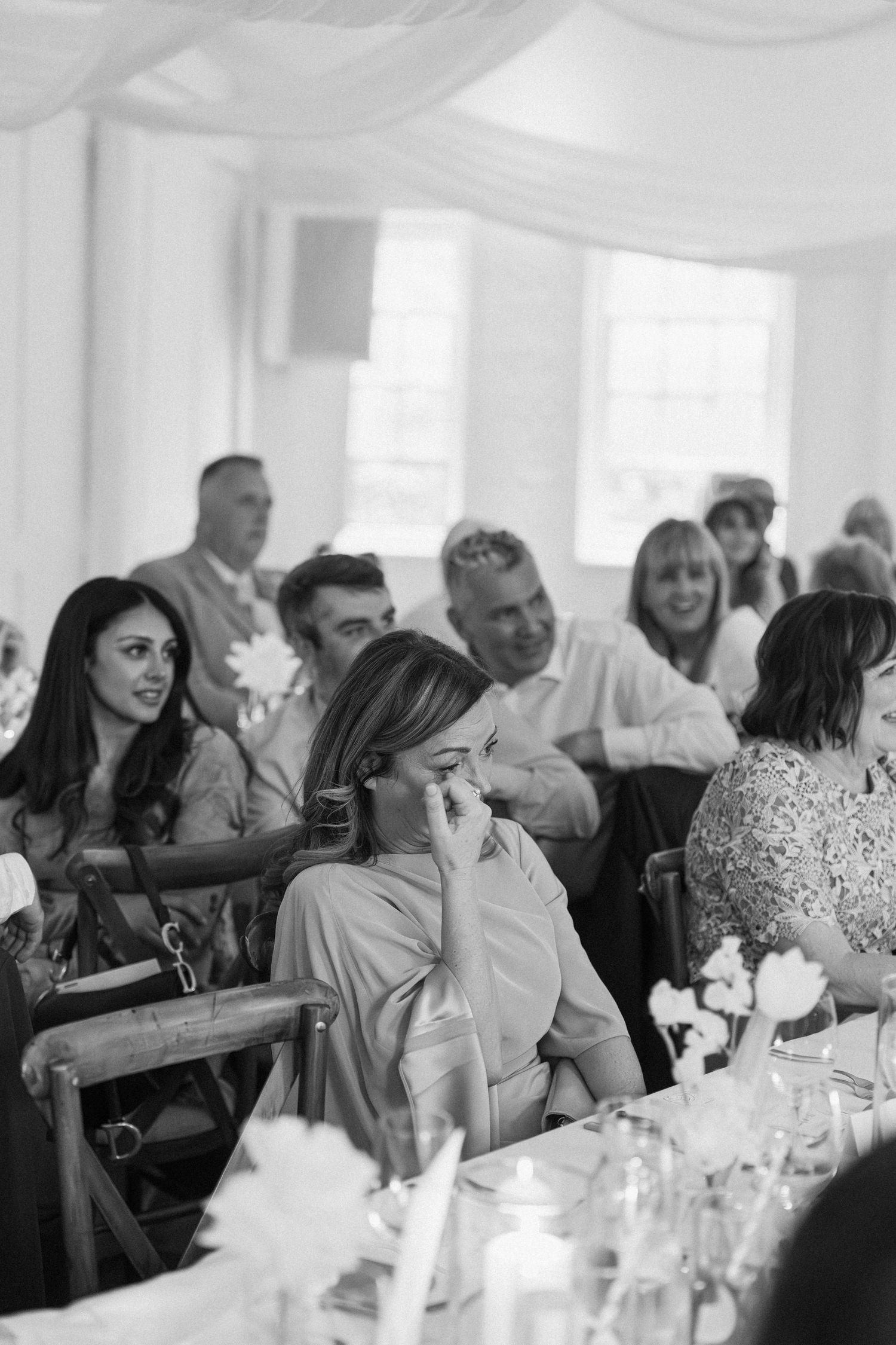 Emotional wedding guest wiping tears during heartfelt speech at elegant white-draped reception venue.