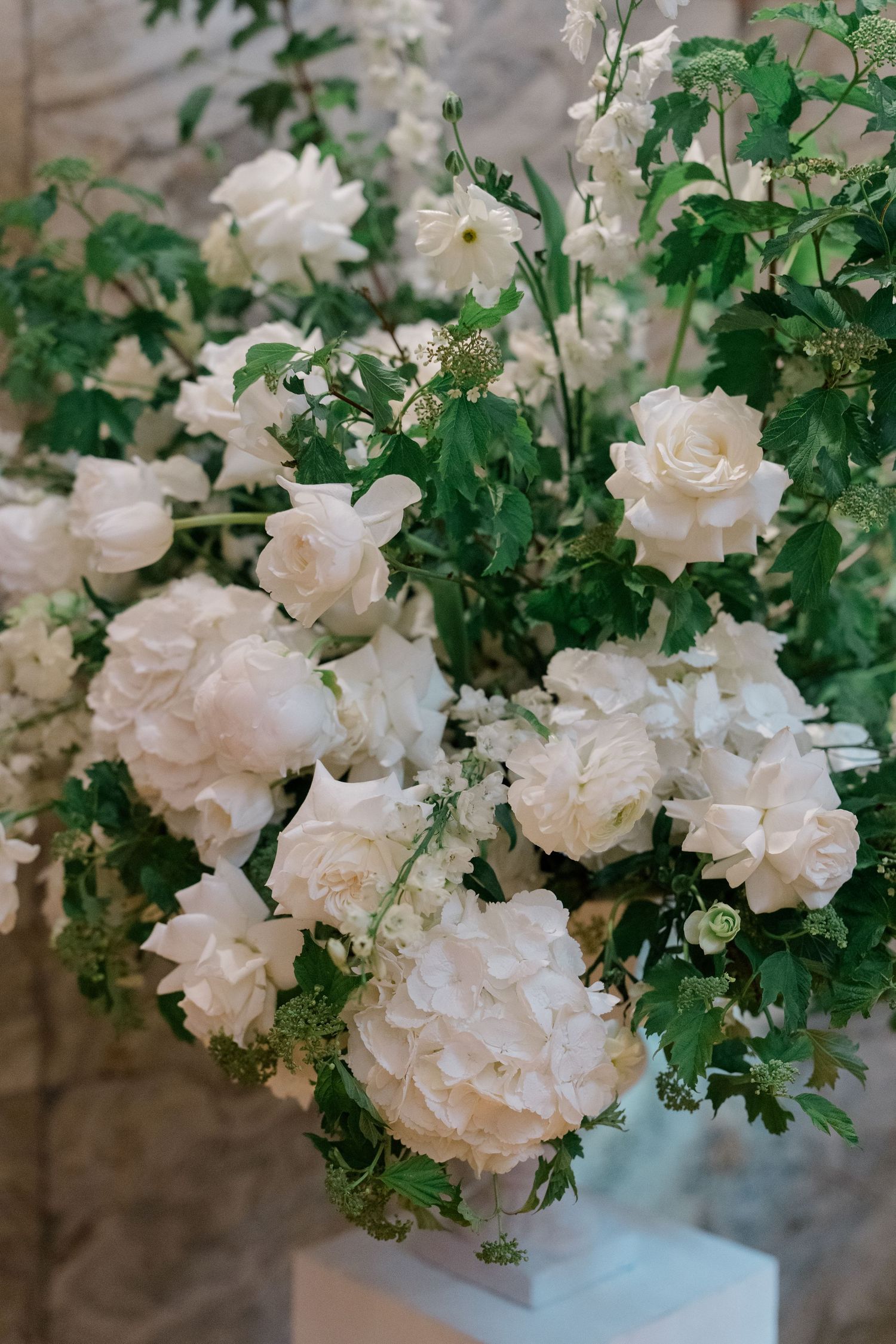 Lush white wedding floral arrangement featuring roses, peonies, and hydrangeas with green foliage.