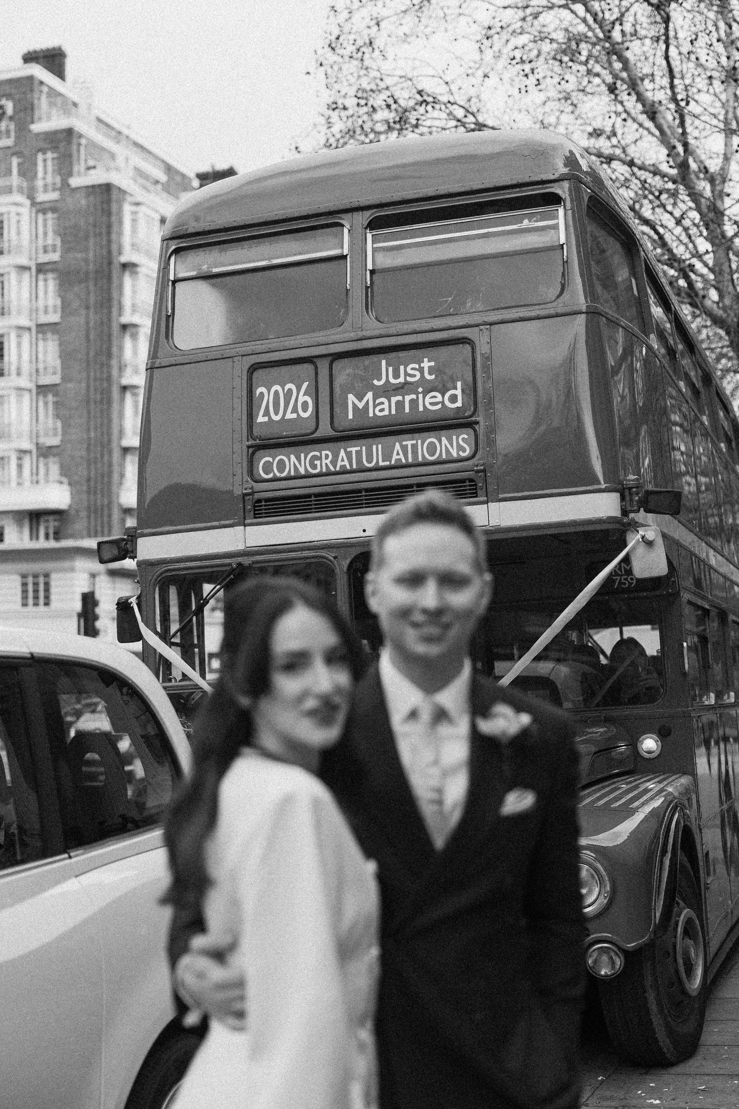 Newlyweds embracing in front of vintage London double-decker bus displaying Just Married sign.
