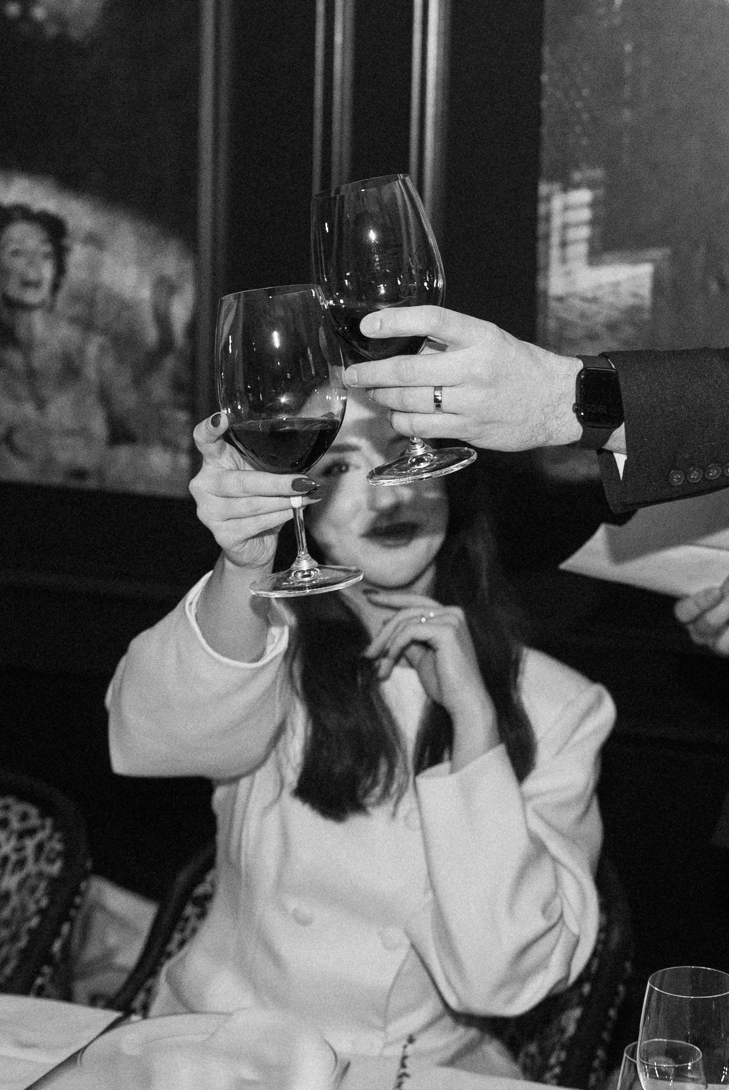 Black and white photo of bride toasting with red wine glasses at wedding reception dinner table.