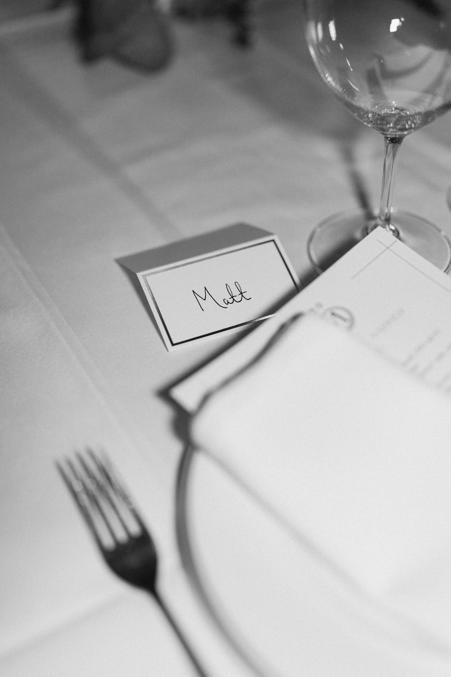 Black and white close-up of elegant wedding place setting with name card reading Matt.