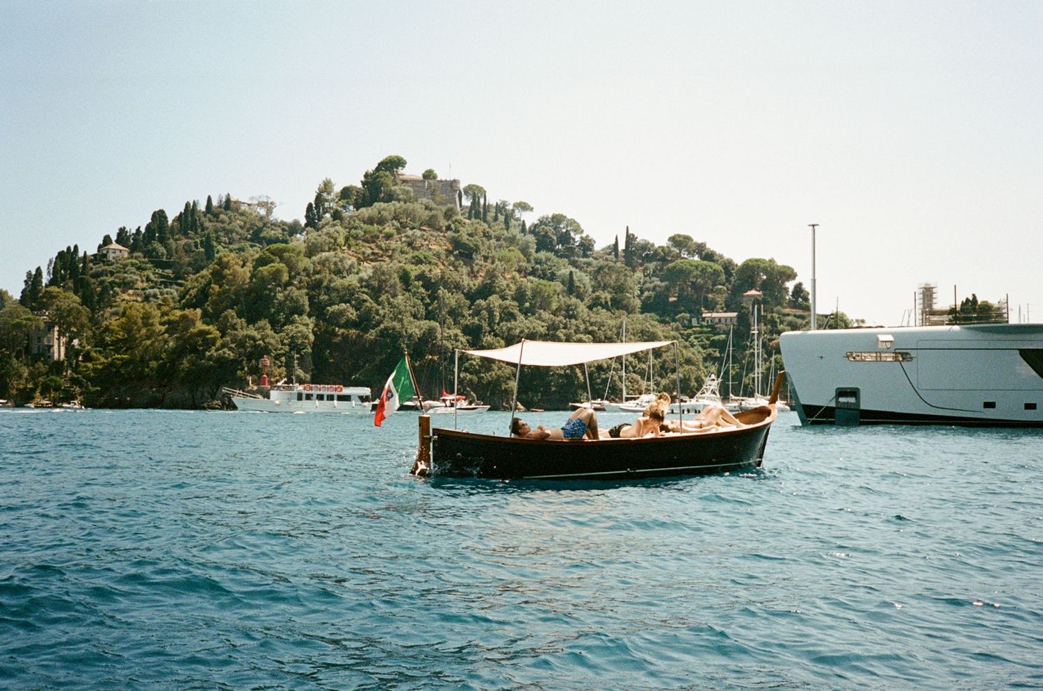 Classic wooden Italian boat with Italian flag cruising near Portofino harbor on a sunny day.