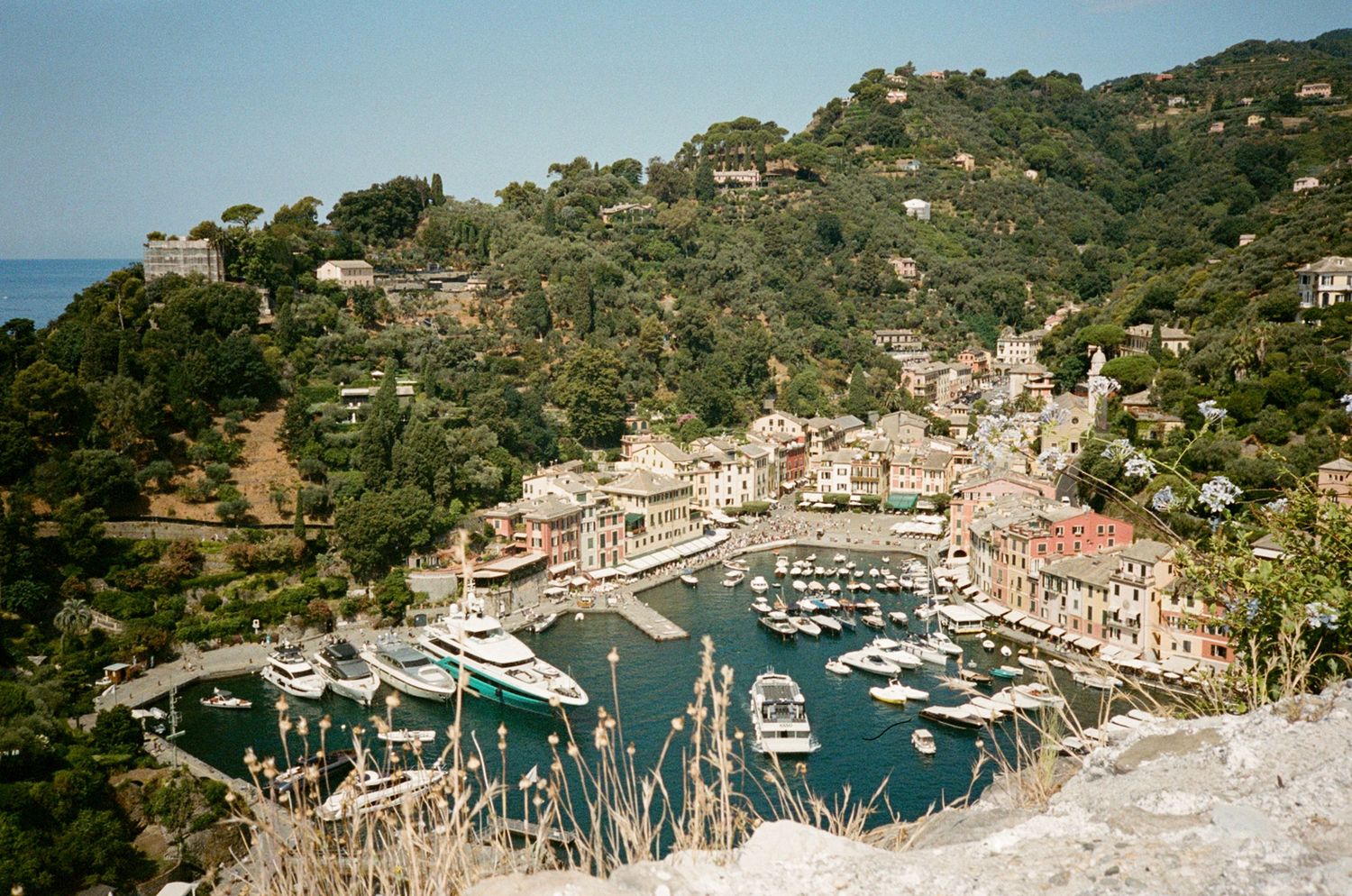 Aerial view of Portofino harbor with colorful buildings, luxury yachts, and lush green hills in Liguria, Italy.