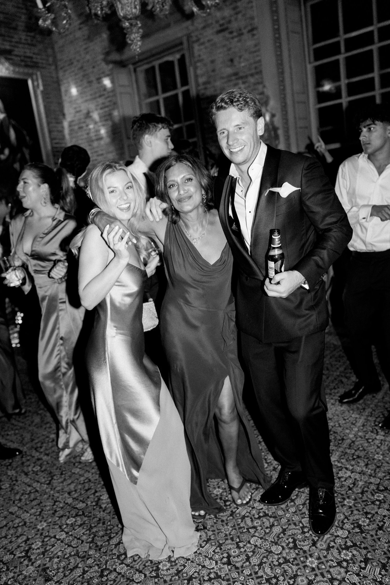 Three wedding guests pose together smiling on outdoor dance floor at evening reception.