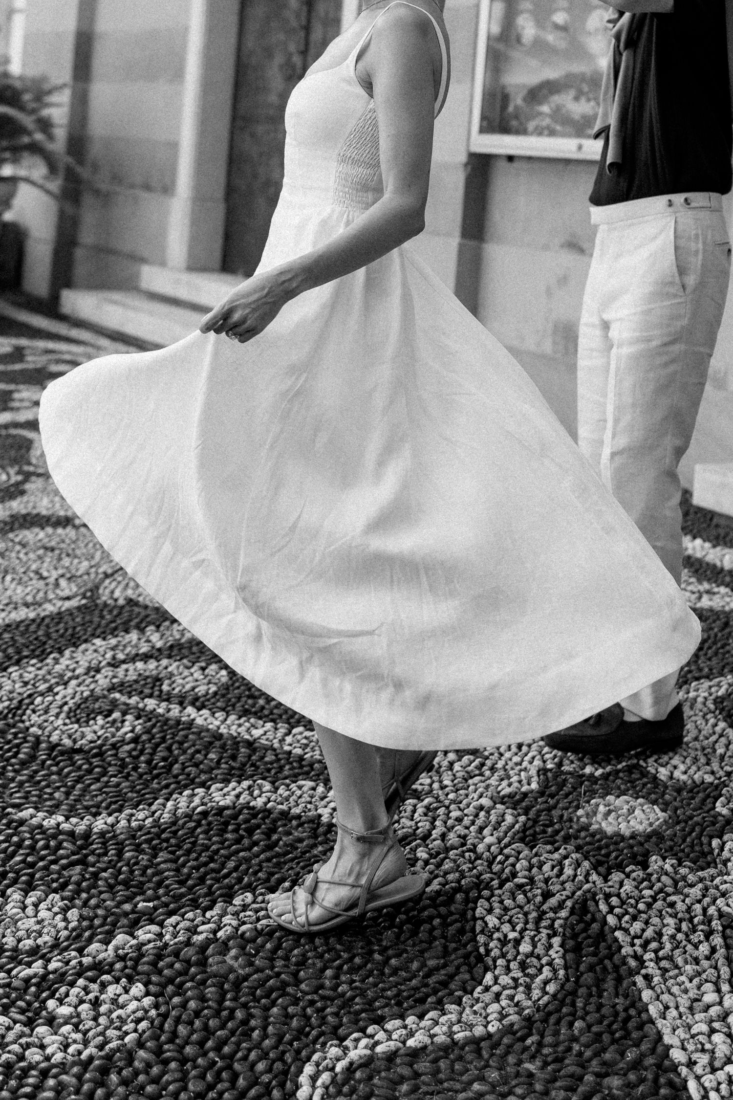 Black and white photo of a woman in a flowing white dress twirling on a decorative mosaic stone pavement.